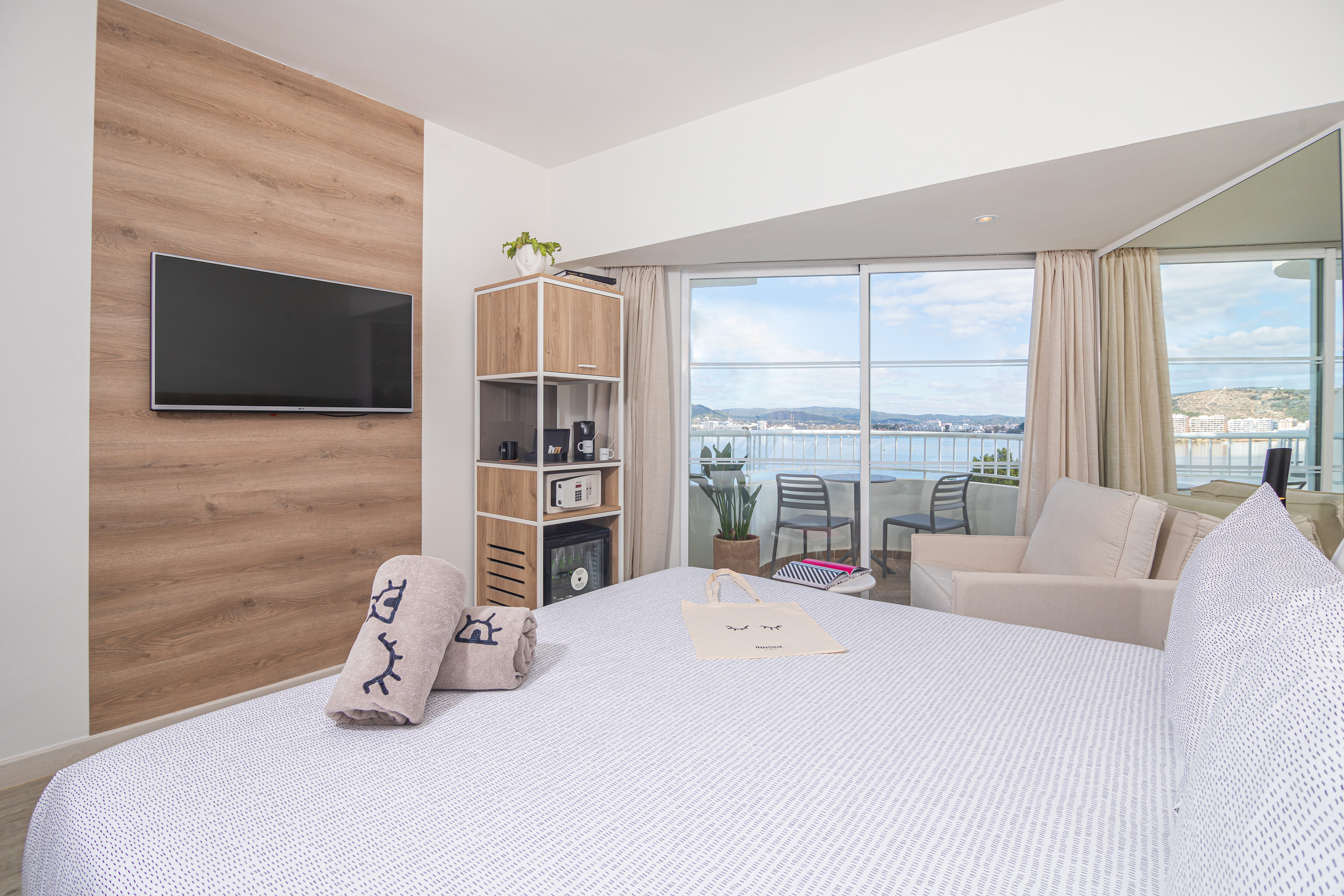 Modern hotel room with bed, TV, and waterfront balcony view.
