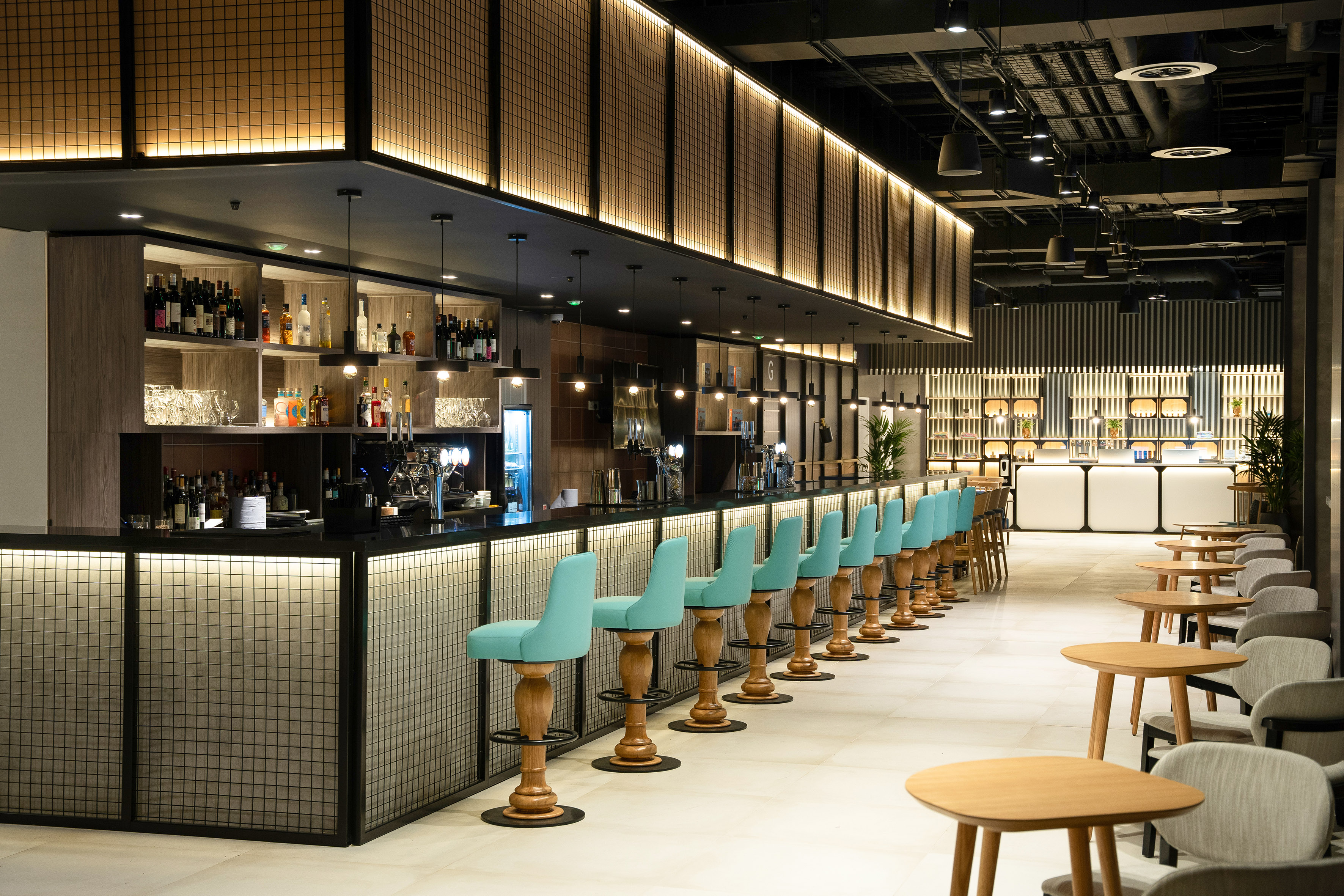 Modern bar with teal stools, illuminated shelving, and lounge seating.