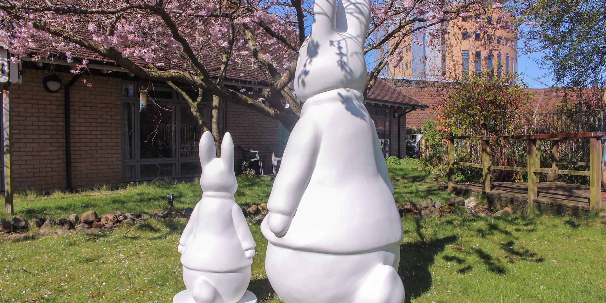 Two white rabbit sculptures in a spring garden under pink cherry blossoms.