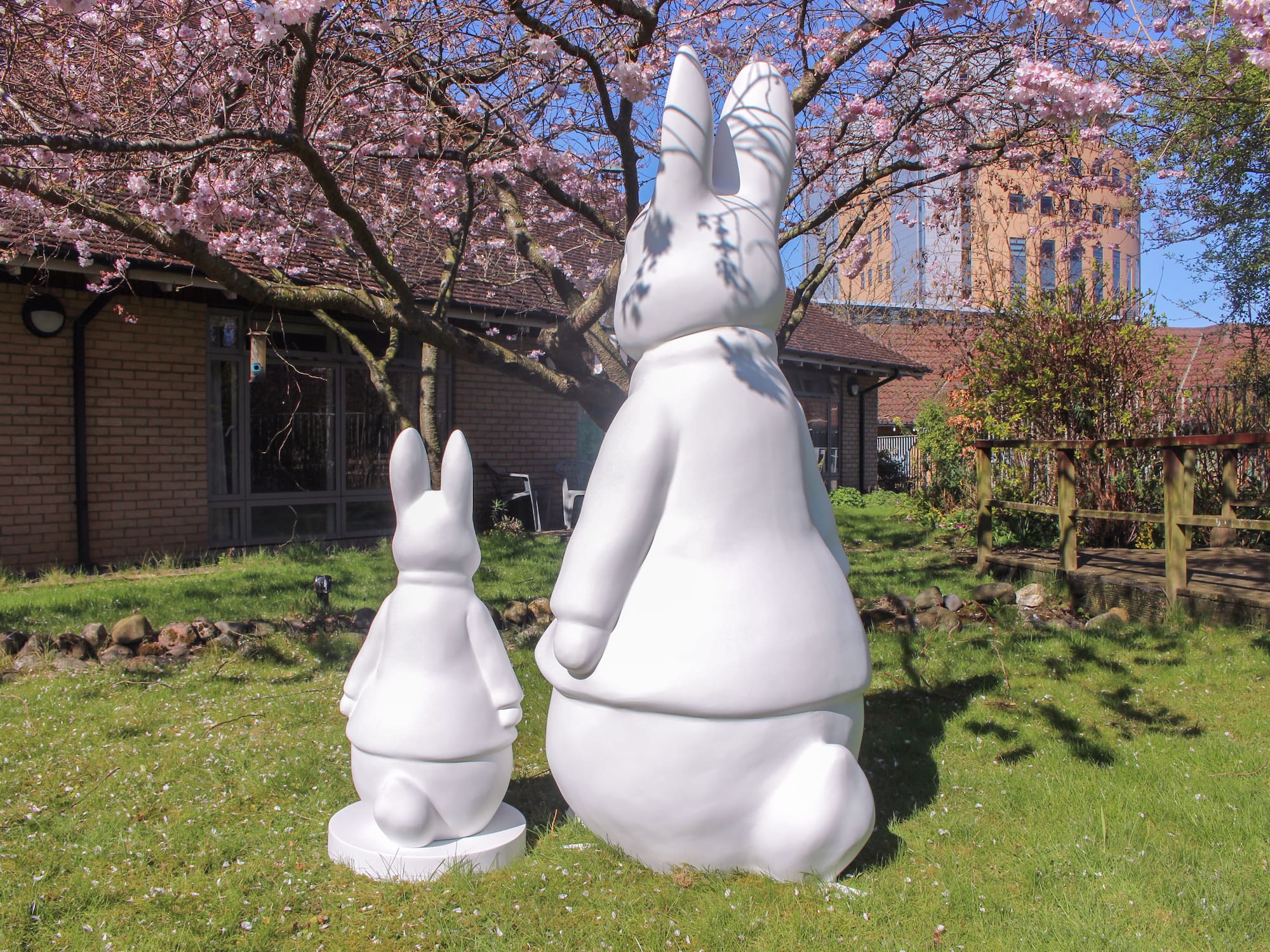 White rabbit sculptures under pink cherry blossoms, spring garden.