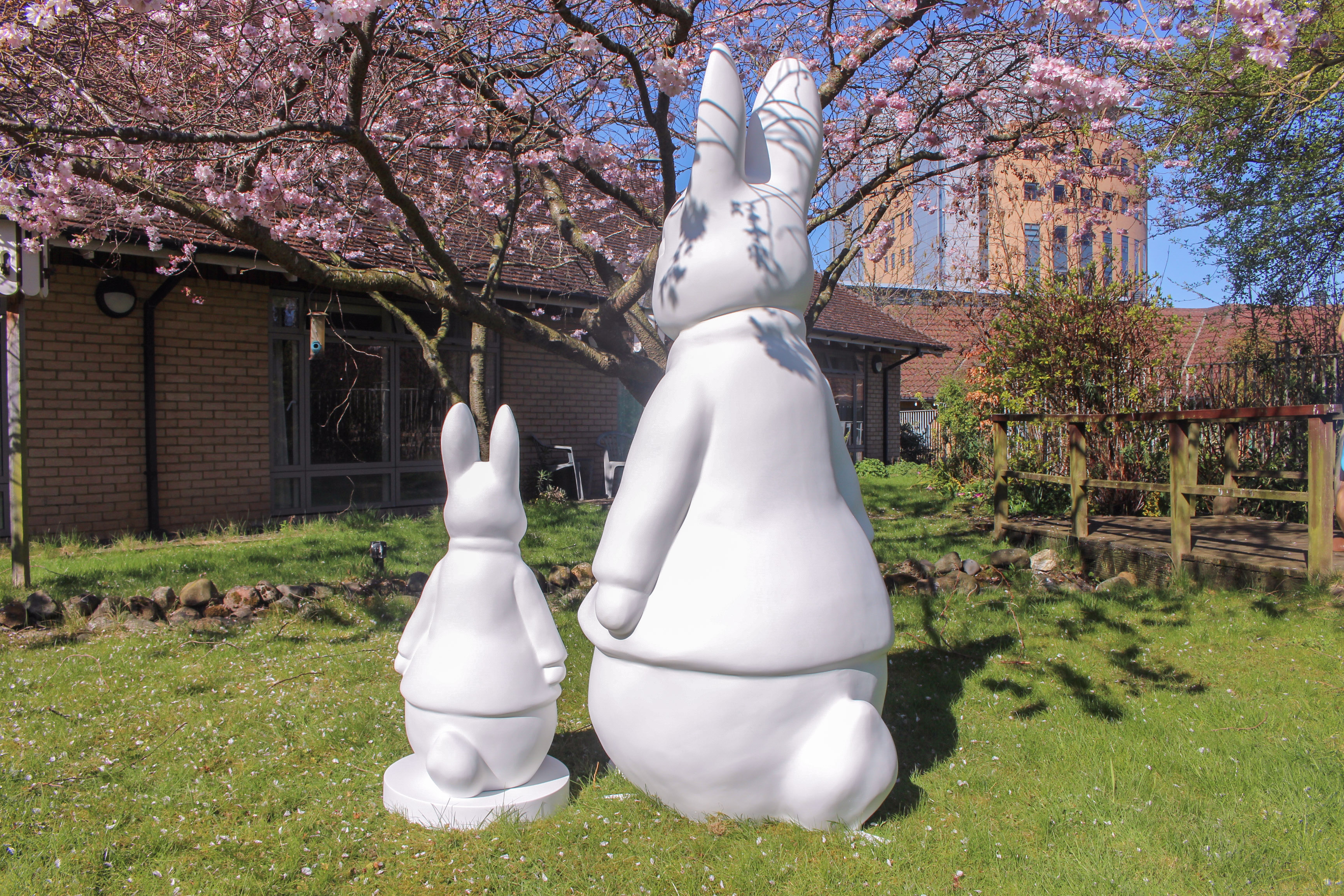 White rabbit sculptures under pink cherry blossoms, spring garden.