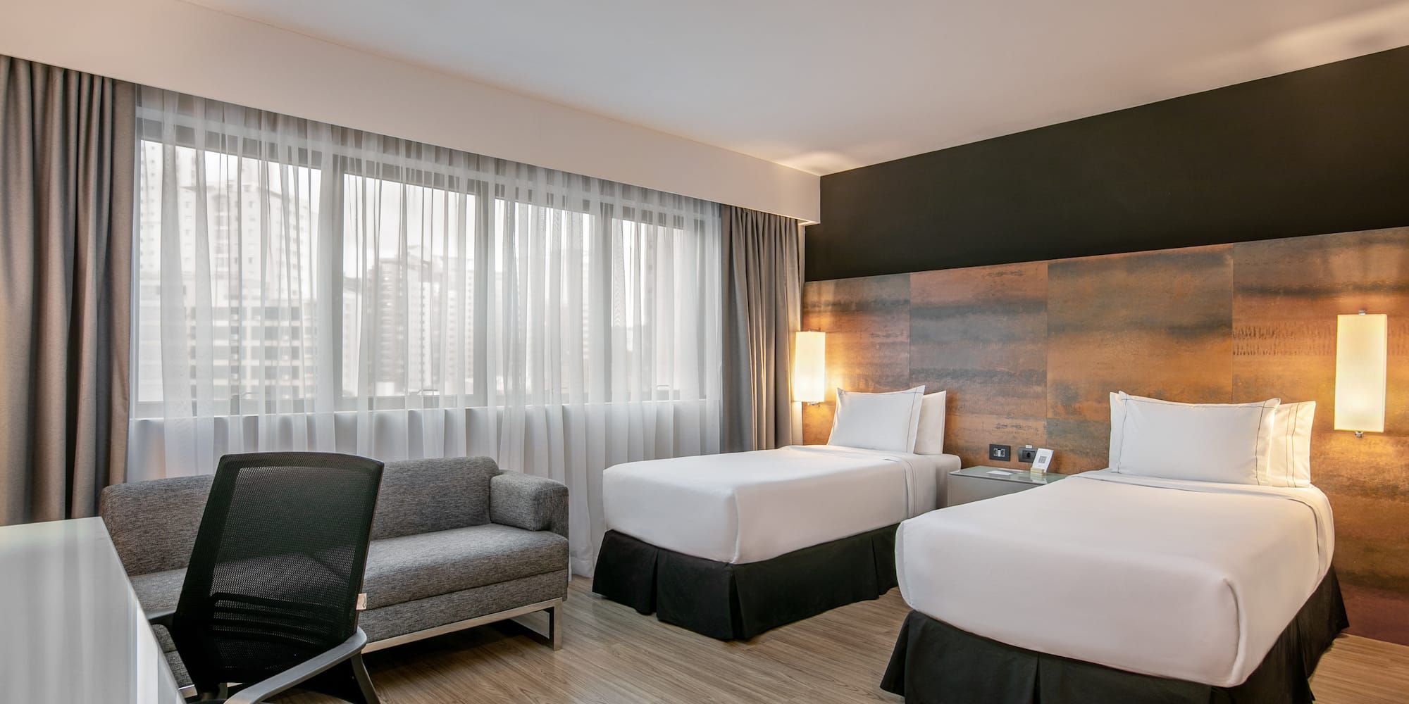 Quarto de hotel moderno com duas camas de solteiro e mesa de trabalho.