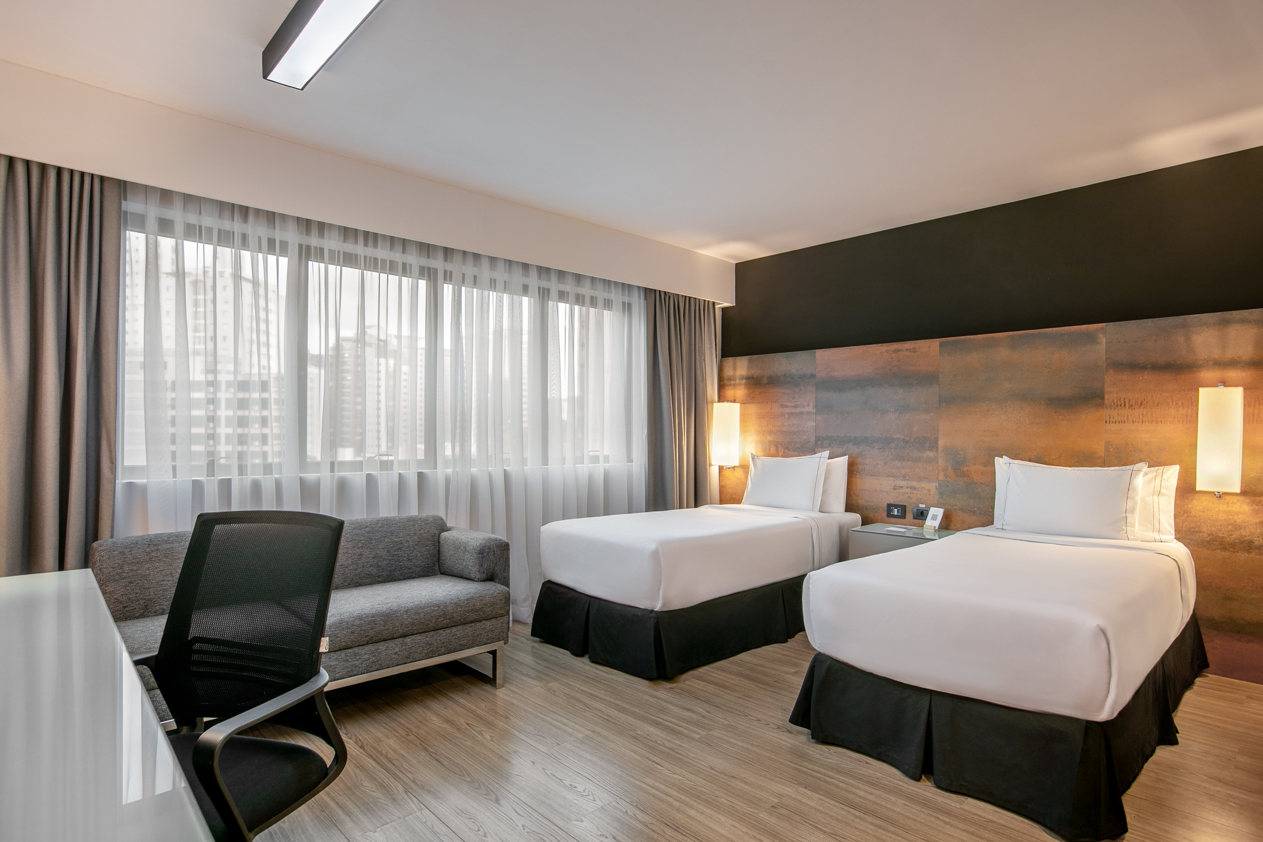 Quarto de hotel moderno com duas camas de solteiro e mesa de trabalho.