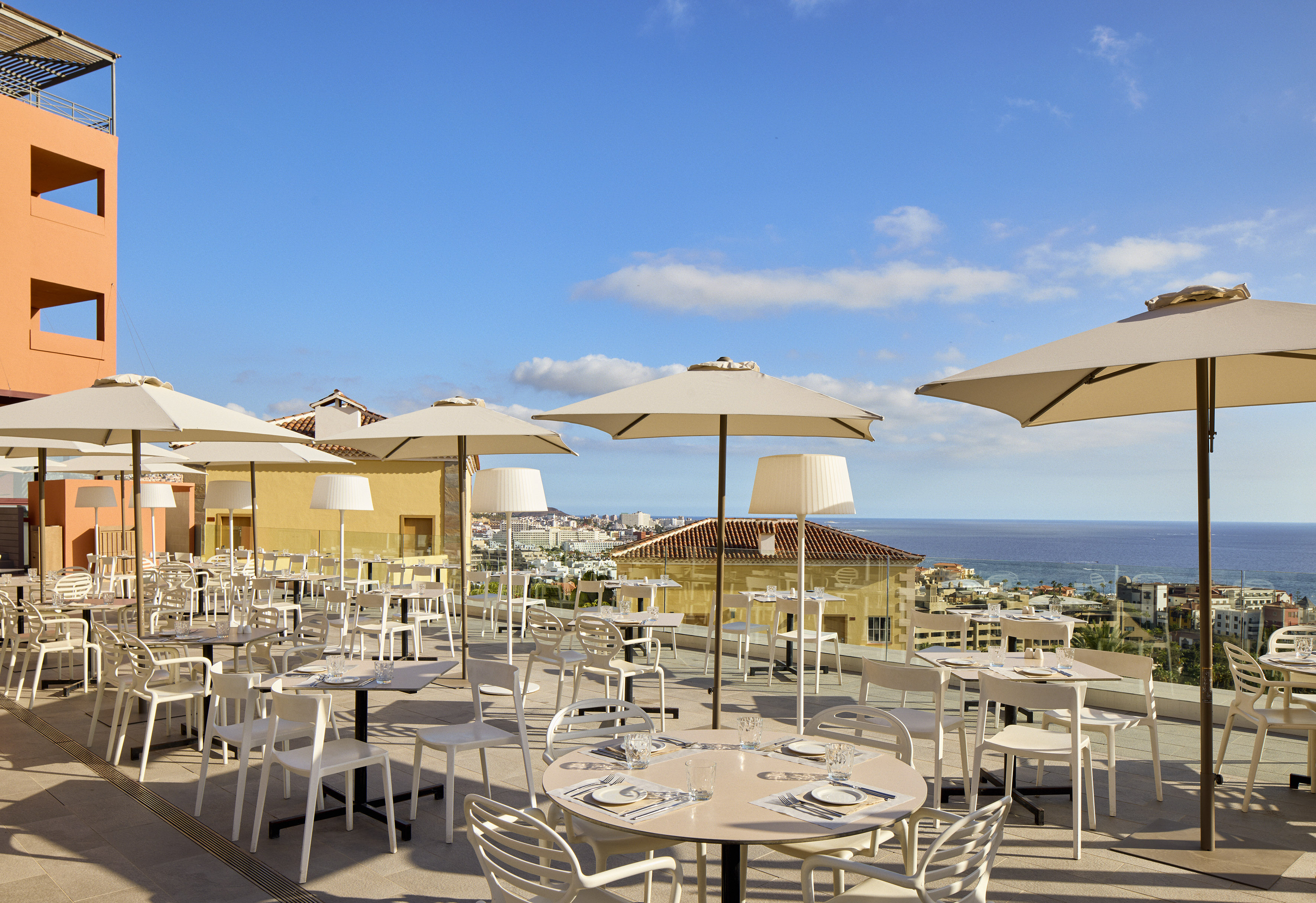 Coastal restaurant terrace with set tables, parasols, and ocean view.