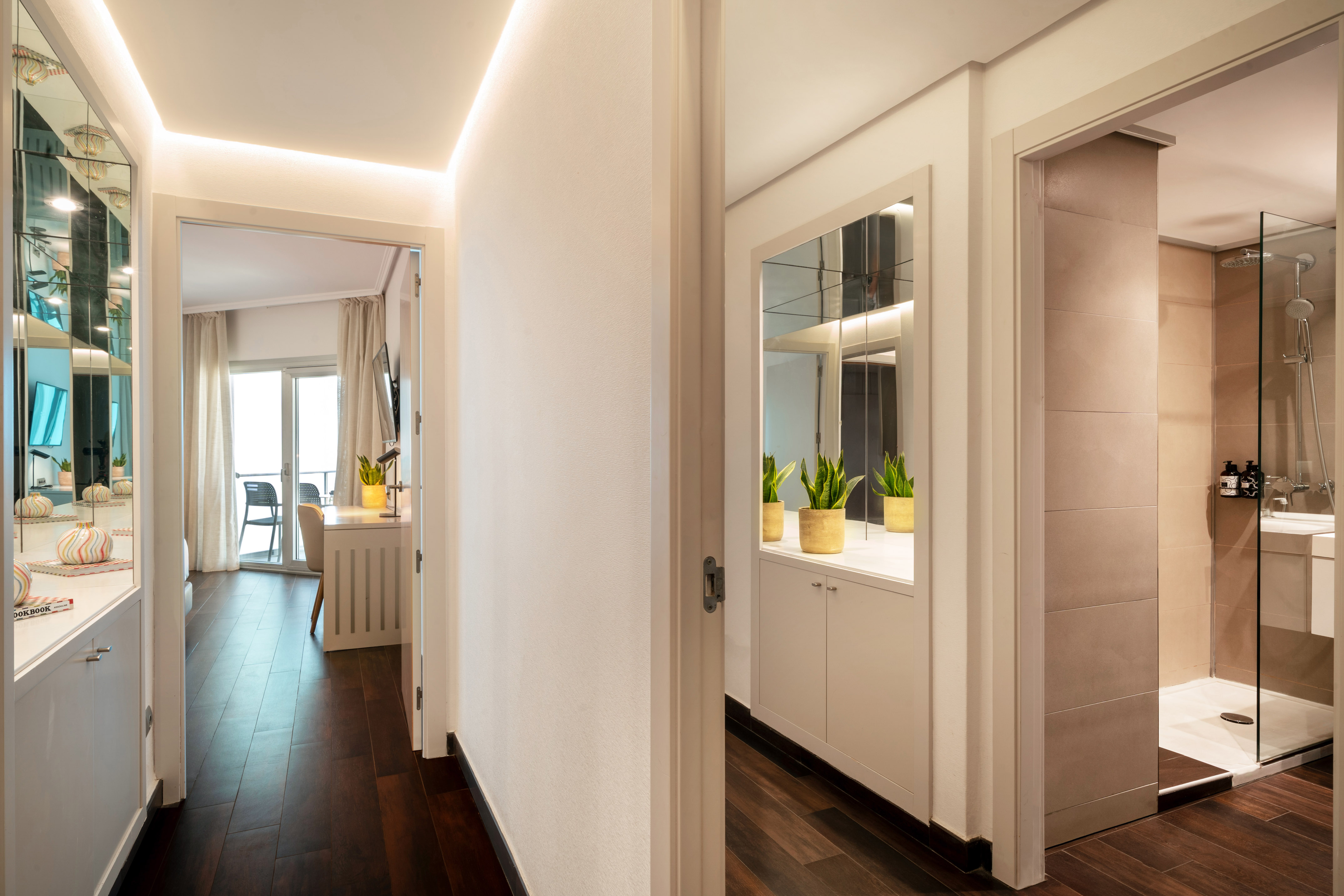 Modern hotel suite hallway with dark wood floor, leading to a bedroom and shower.