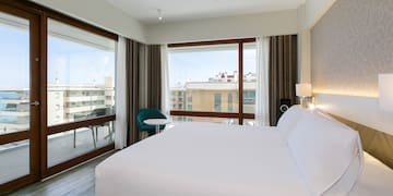 a bed with white sheets and a chair in a room with windows