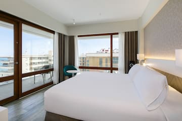 a bed with white sheets and a chair in a room with windows