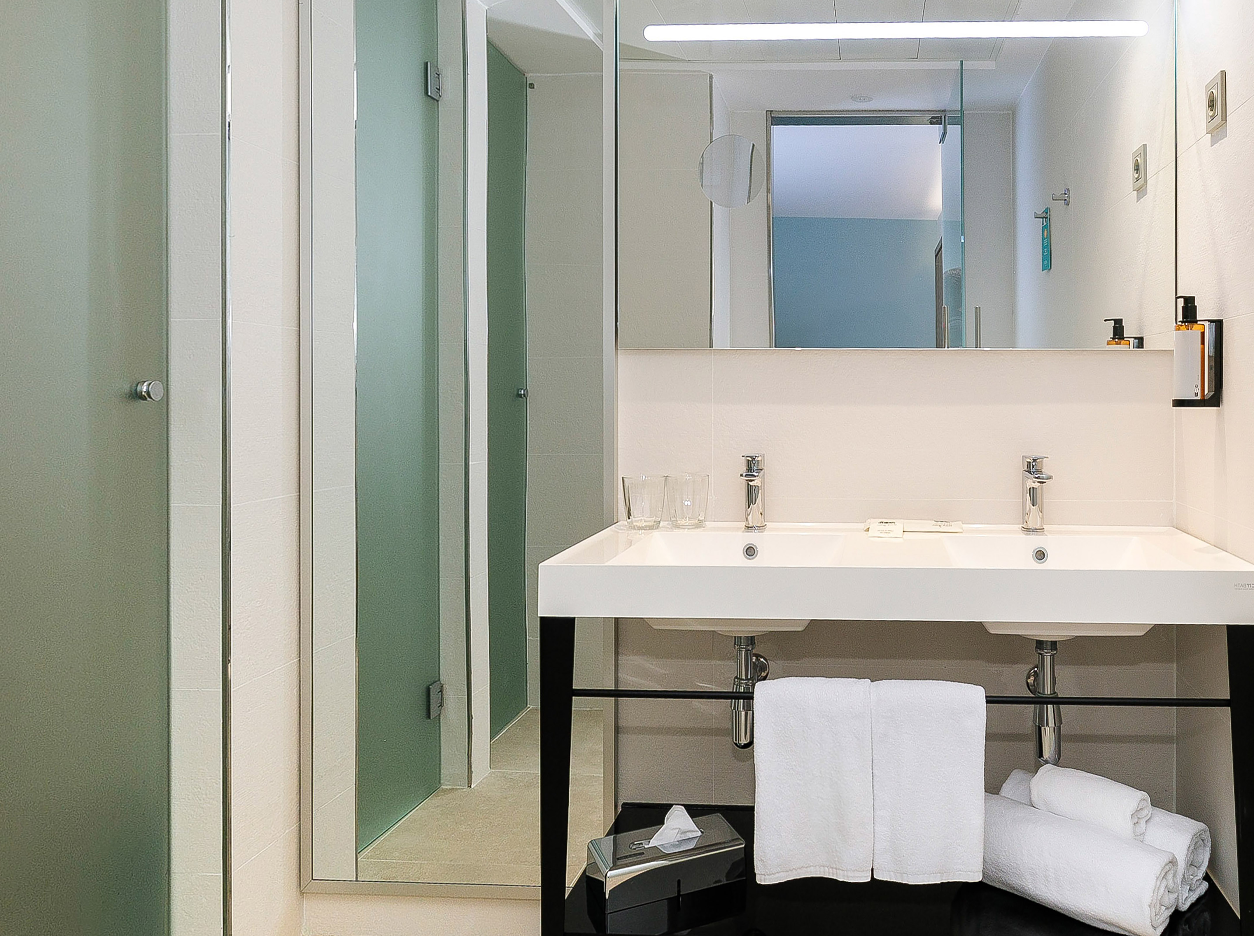 Modern bathroom with dual sinks, large mirror, and frosted glass shower.