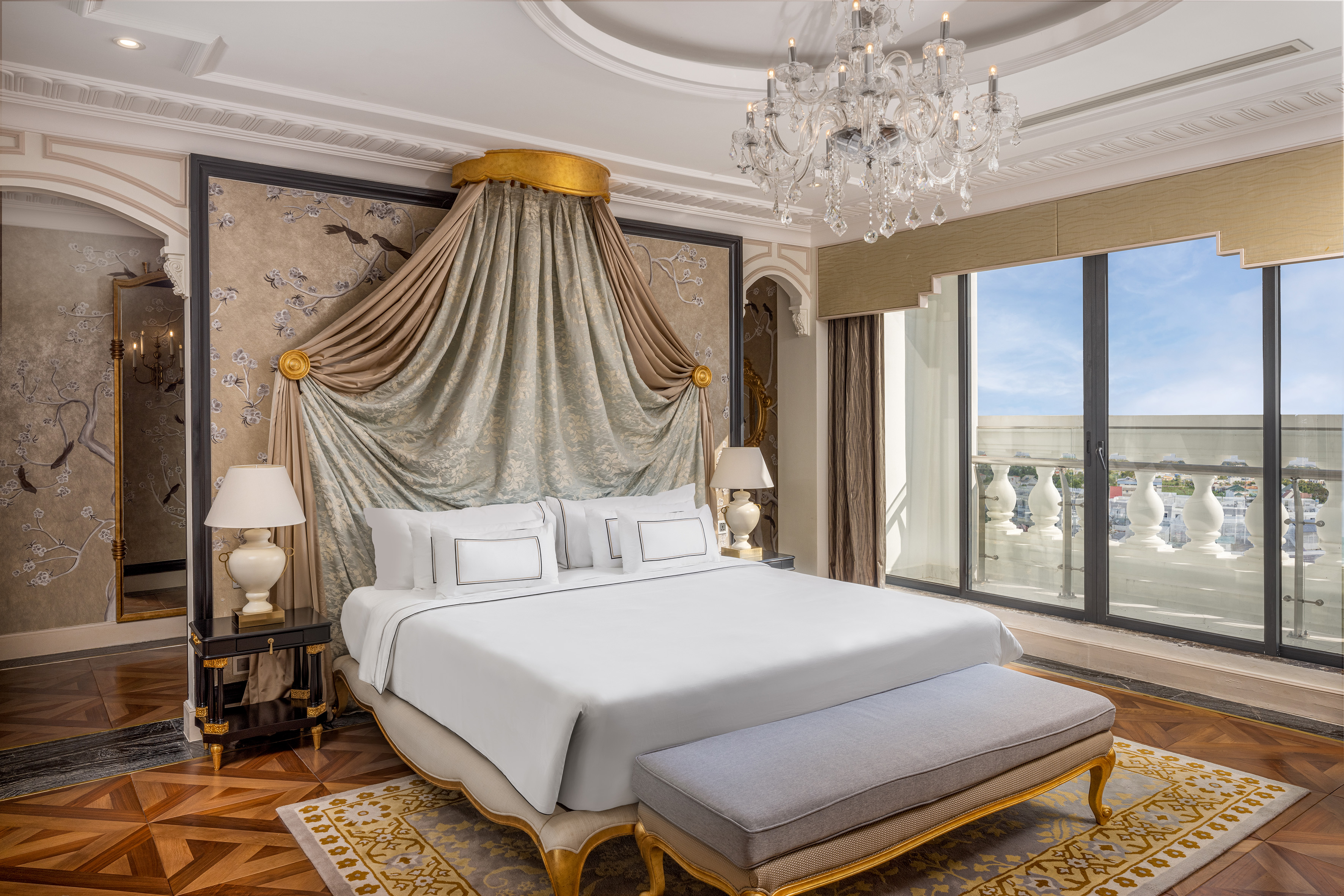 Elegant luxury bedroom with draped king bed, crystal chandelier, and balcony.