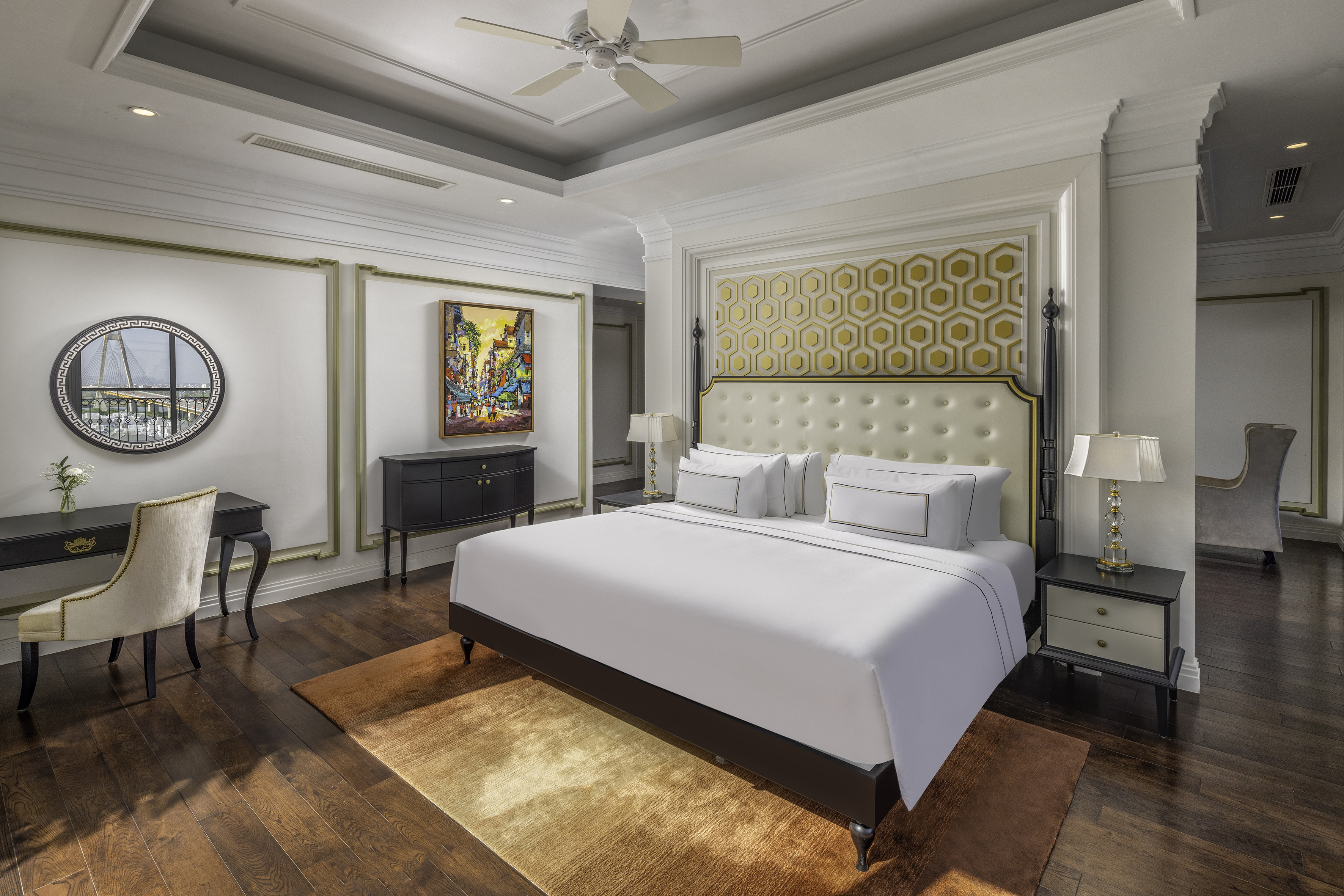 Elegant hotel bedroom with white bed, gold geometric headboard, dark wood floors.