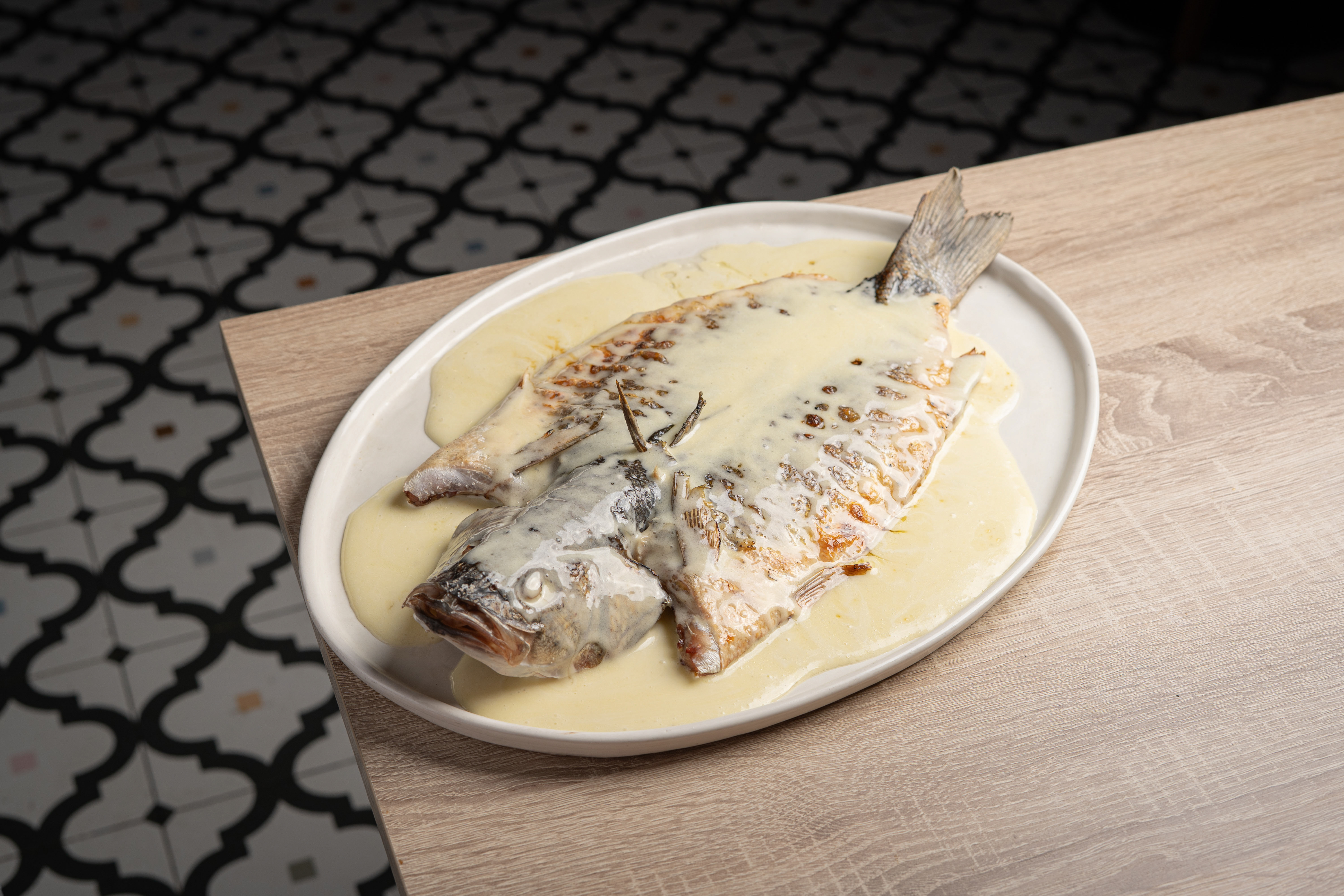 Baked whole fish in cream sauce with rosemary on a white platter.