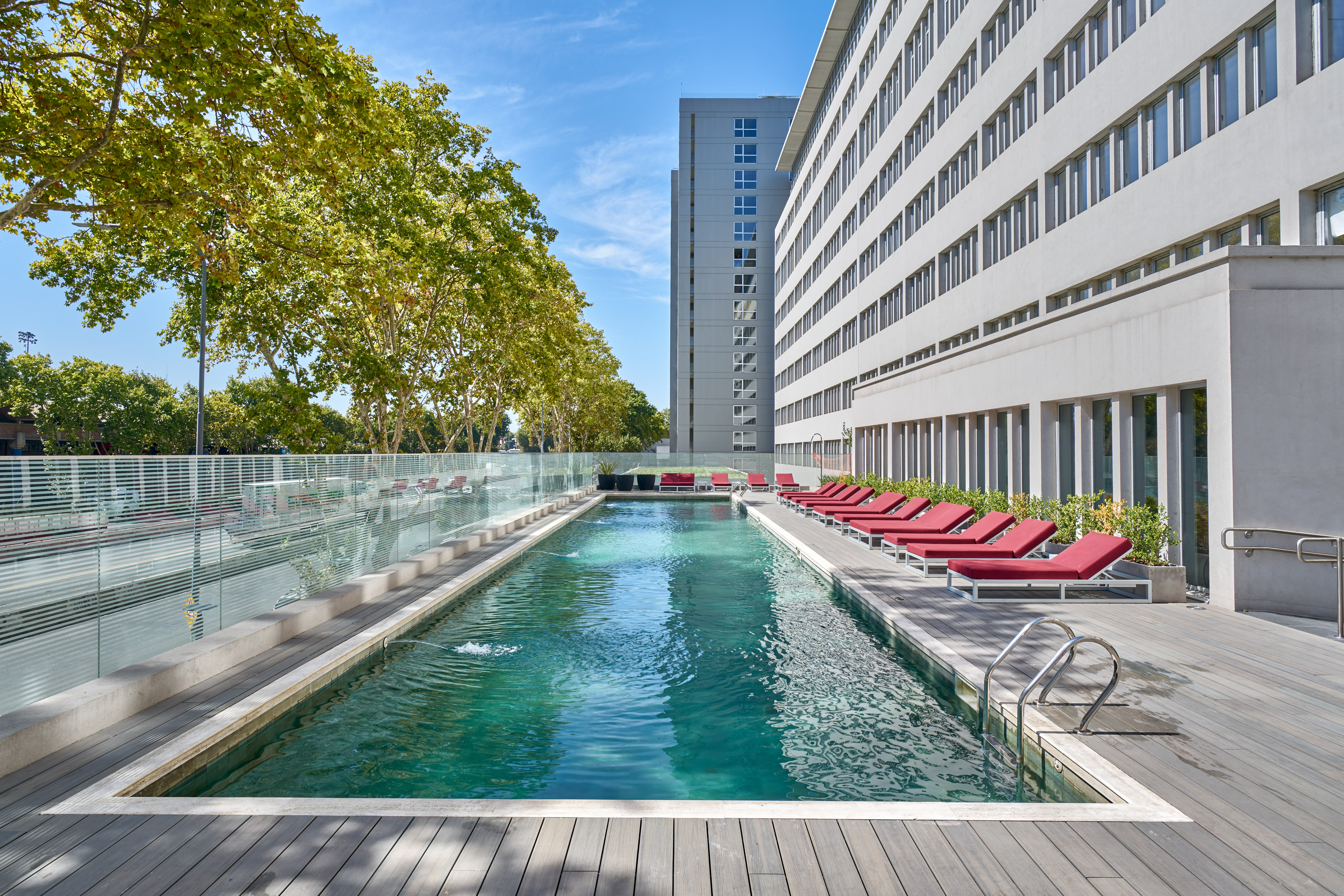 Rooftop pool with red lounge chairs, wood deck, and modern building.