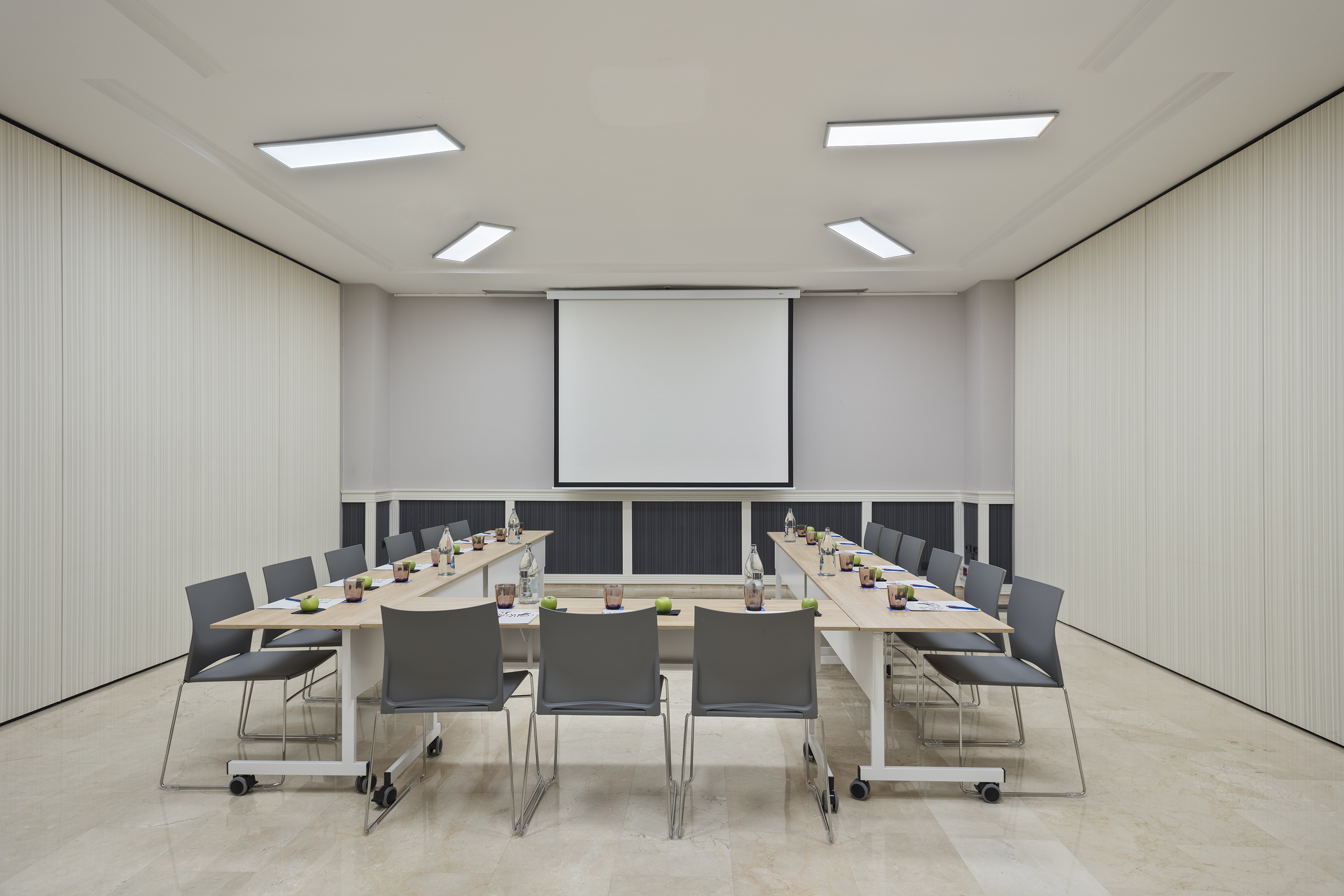Modern conference room with U-shaped table, chairs, and projector screen.