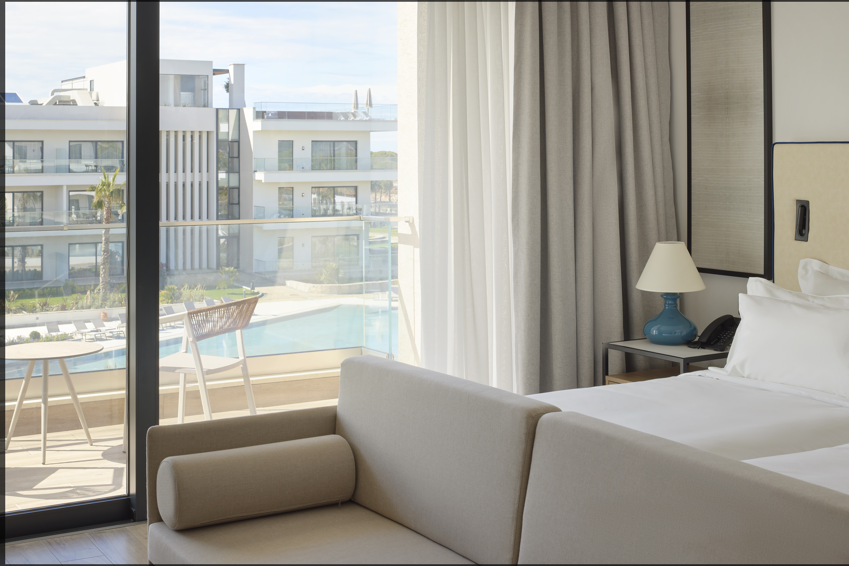 Modern hotel room with balcony, pool view, and resort buildings.