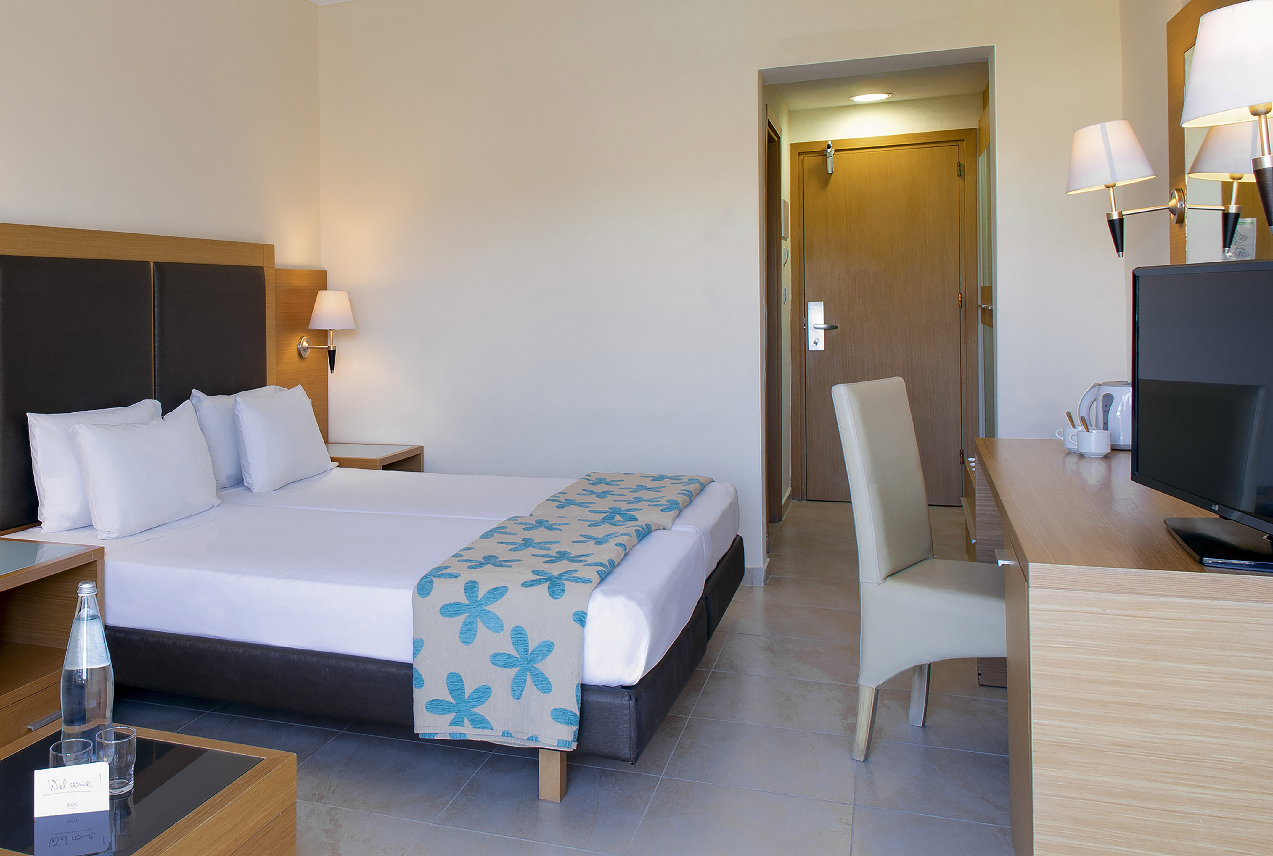 Modern hotel room with a large bed, desk, TV, and two bedside lamps.