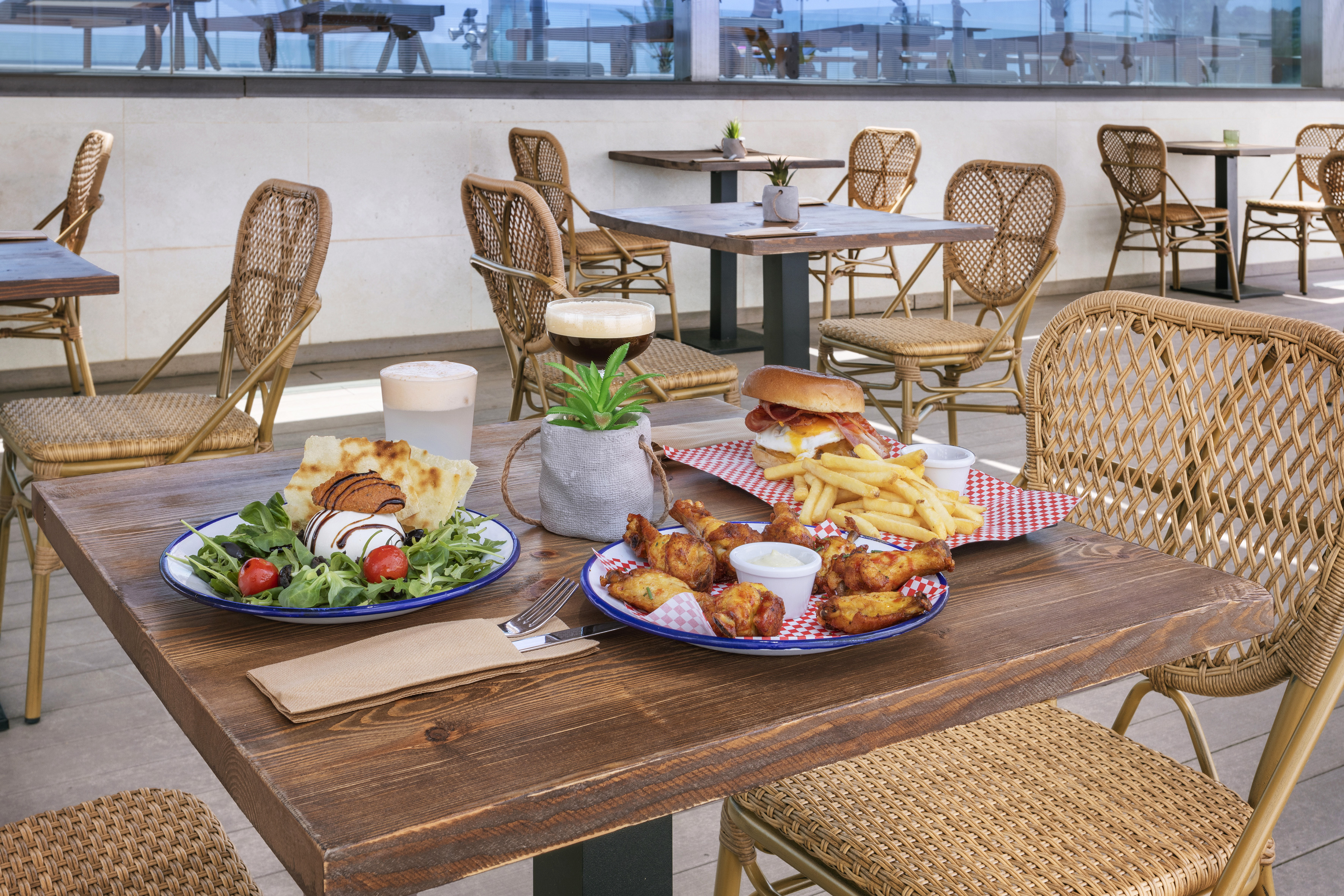 Outdoor cafe table with burger, fries, chicken wings, and fresh salad.