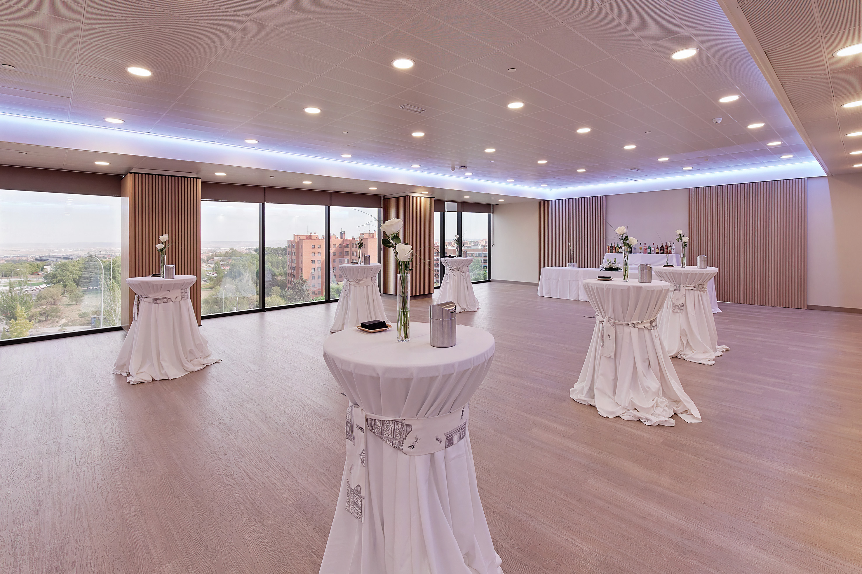 Modern event room with white cocktail tables, large windows, and city view.