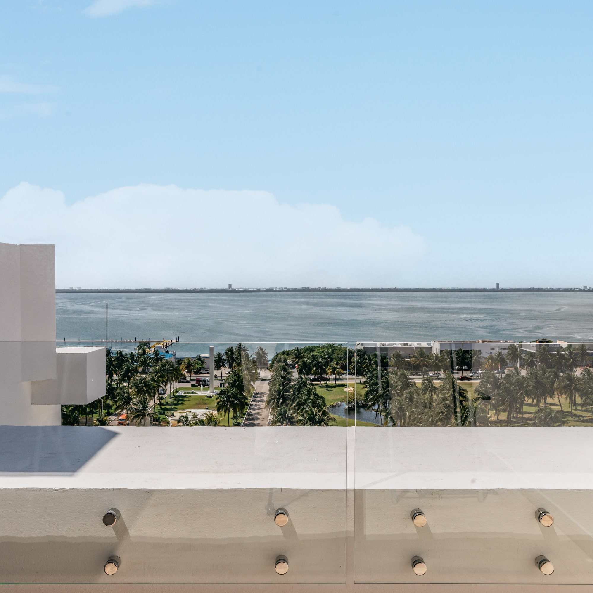 Balcony with glass railing overlooking bay, palm trees, and distant city skyline.