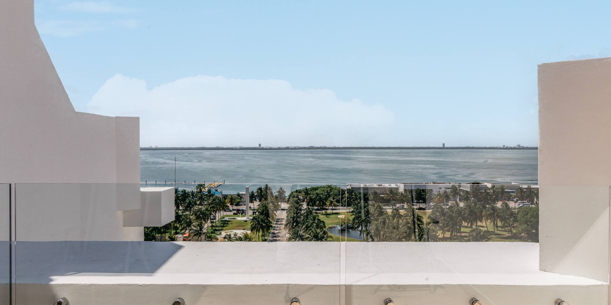Balcony with glass railing overlooking bay, palm trees, and distant city skyline.