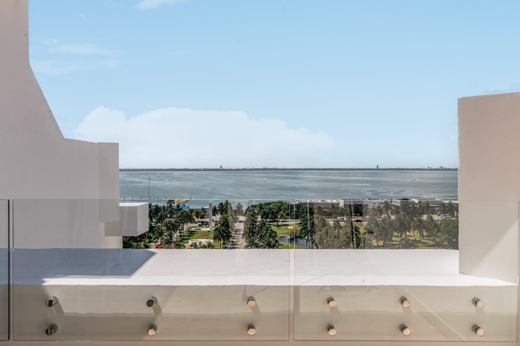 Balcony with glass railing overlooking bay, palm trees, and distant city skyline.
