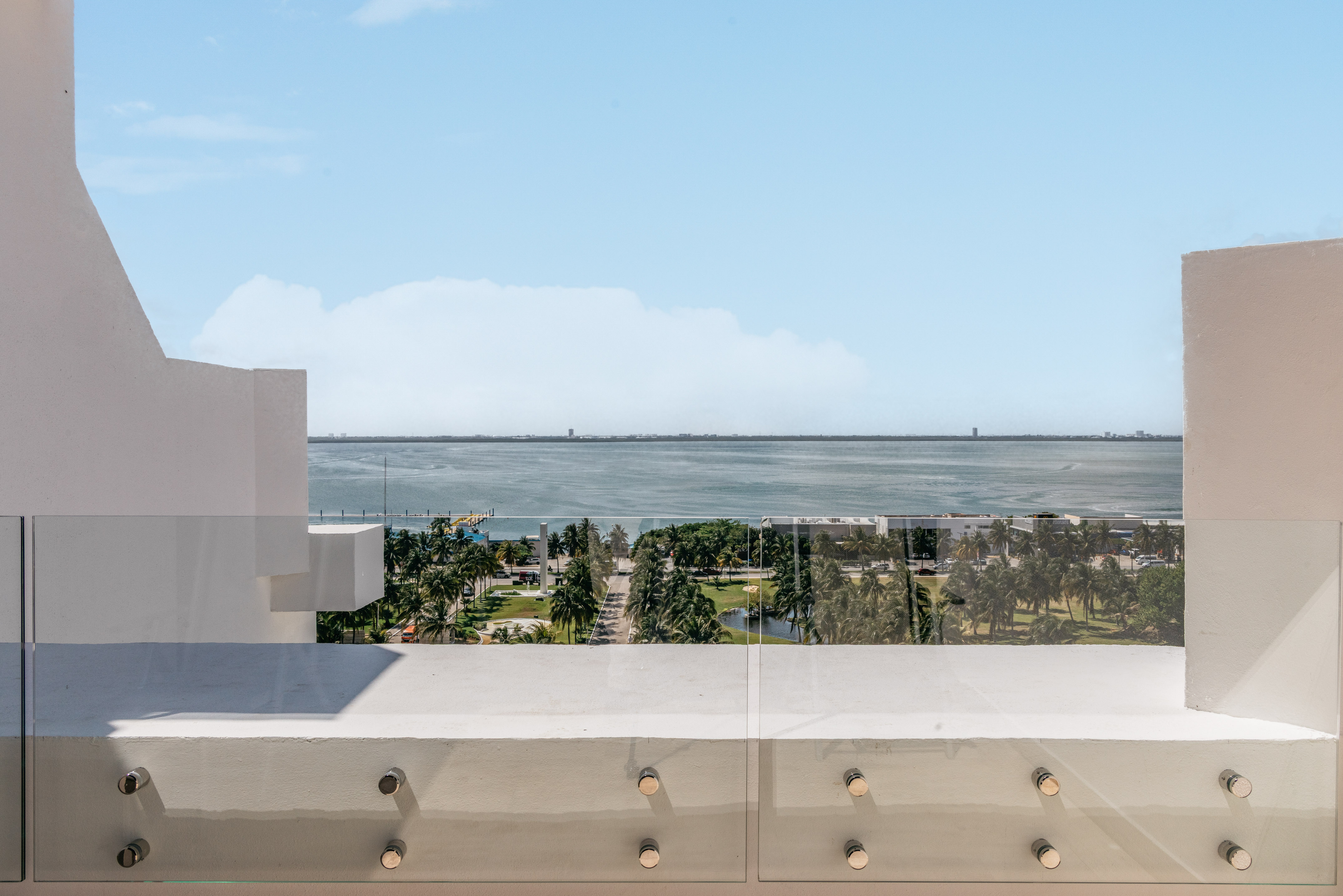 Balcony with glass railing overlooking bay, palm trees, and distant city skyline.