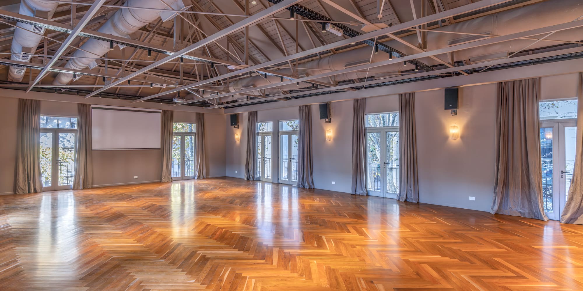 Spacious event venue with herringbone wood floor, exposed ceiling, and French doors.