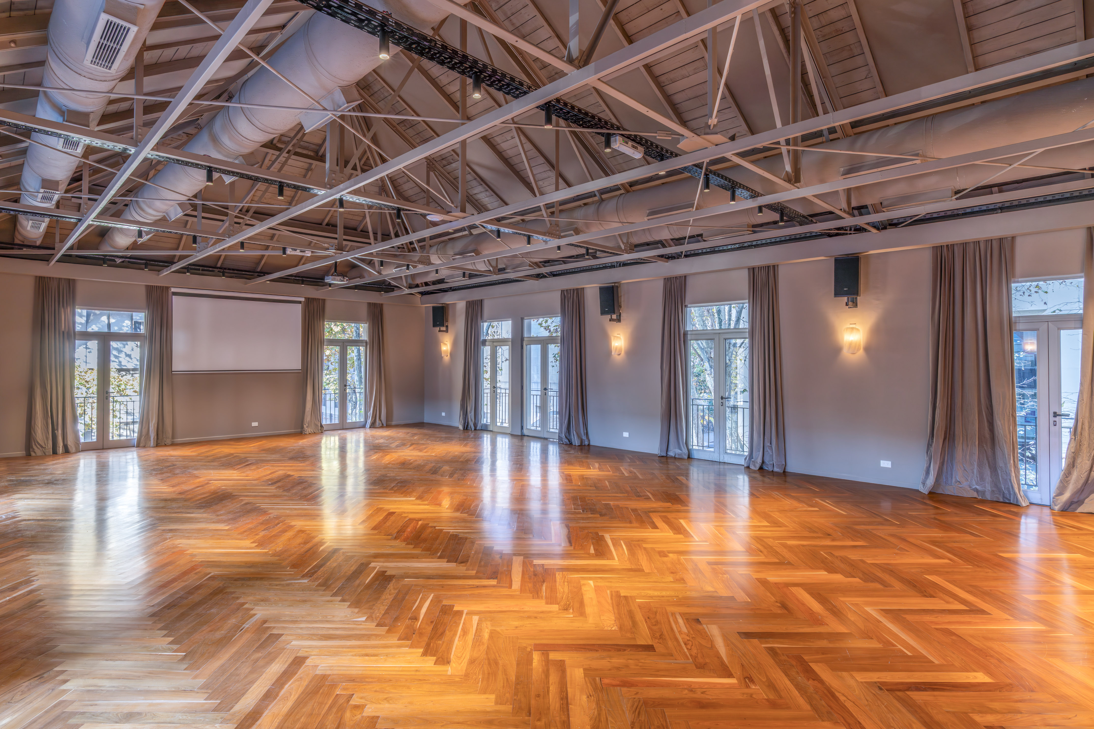Spacious event venue with herringbone wood floor, exposed ceiling, and French doors.