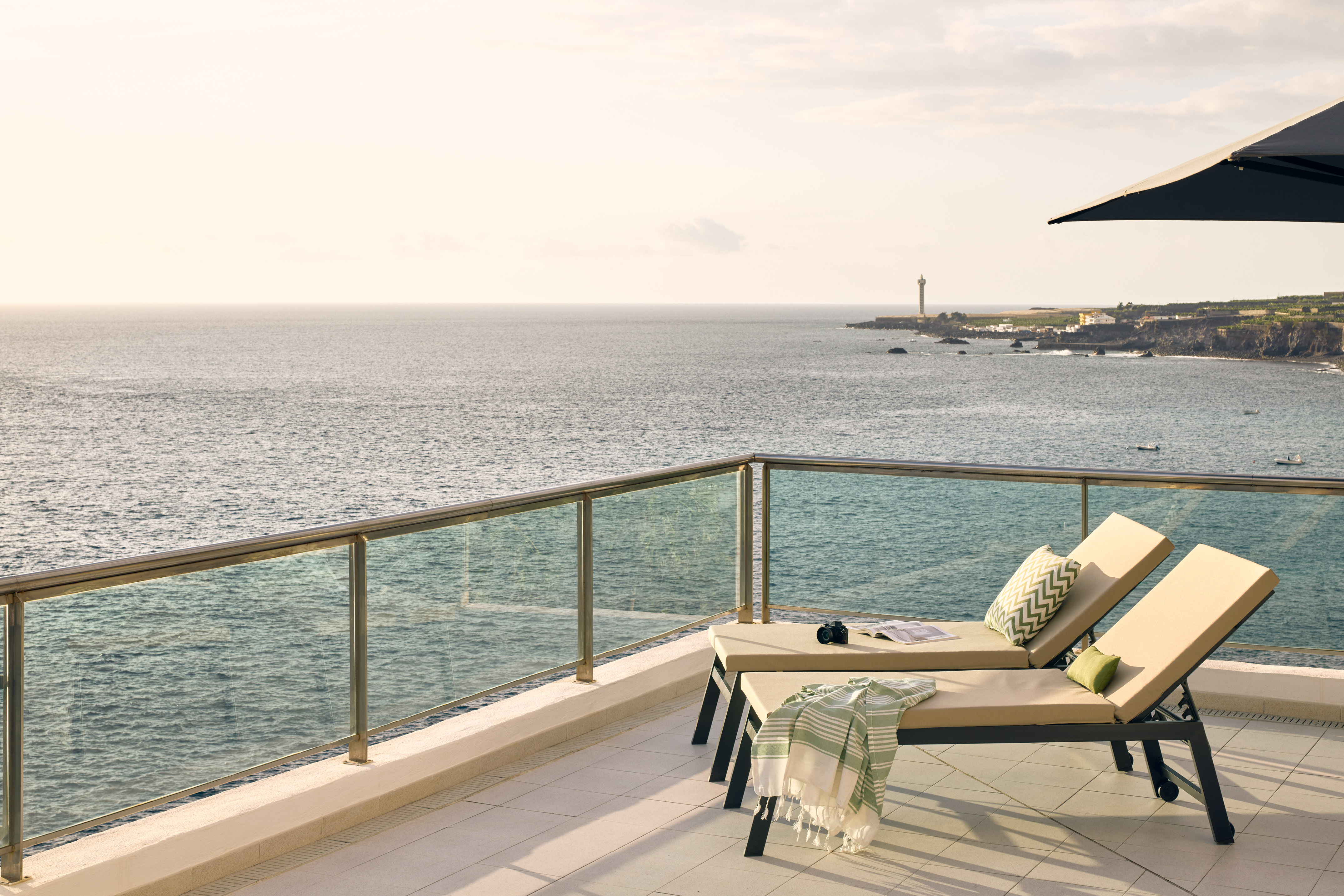 Ocean view terrace with lounge chairs and coastal lighthouse.