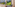Balcony with lounge chairs, modern white buildings on a lush green hillside.