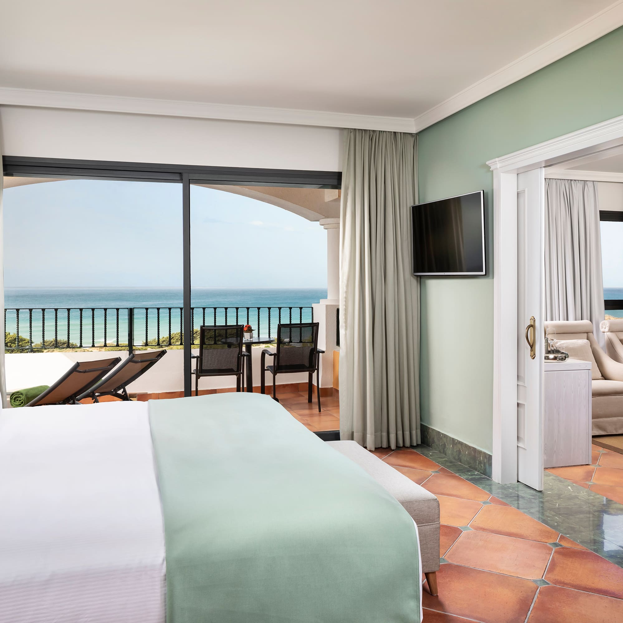 a room with a bed and a television and a balcony overlooking the ocean