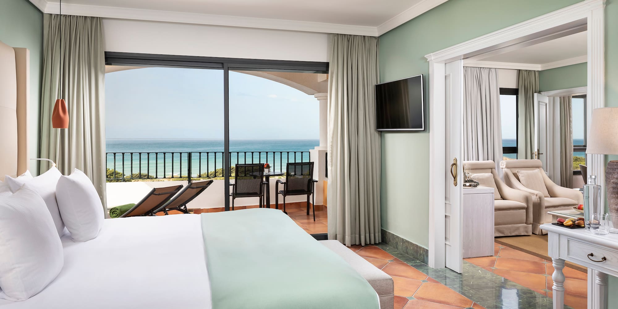 a room with a bed and a television and a balcony overlooking the ocean
