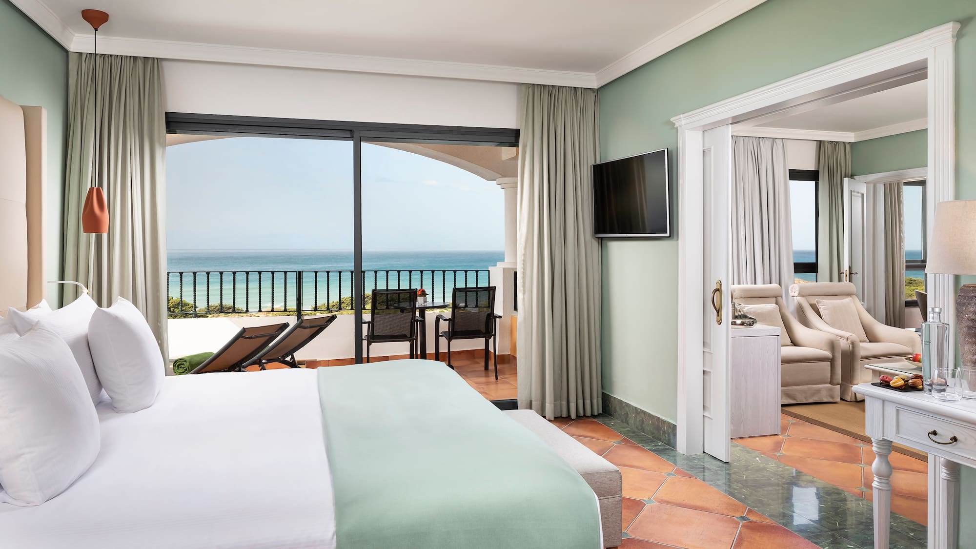 a room with a bed and a television and a balcony overlooking the ocean