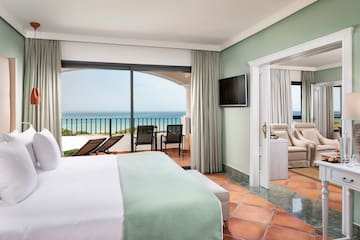 a room with a bed and a television and a balcony overlooking the ocean