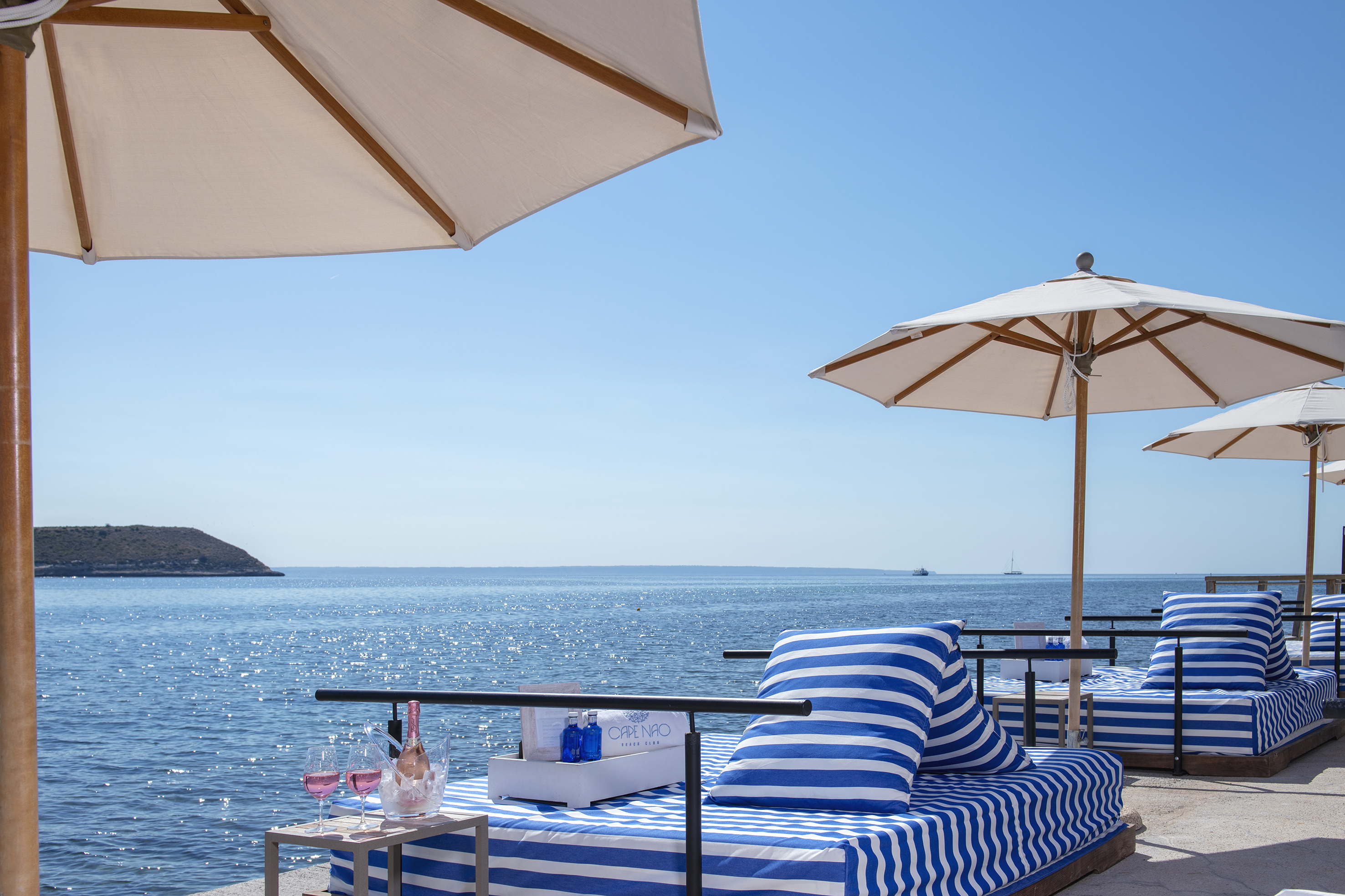 Beach club daybeds, umbrellas, blue ocean view, and rosé wine.