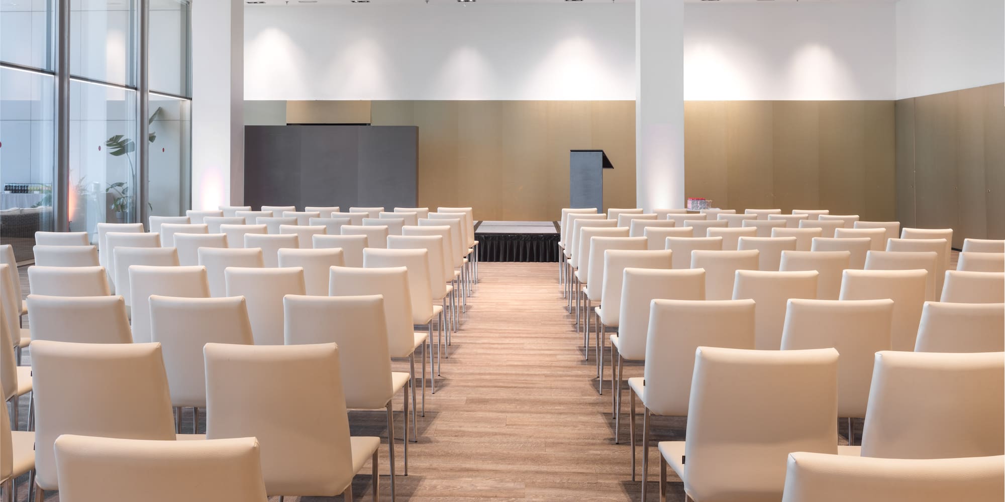 Spacious conference room with rows of white chairs, stage, and podium.