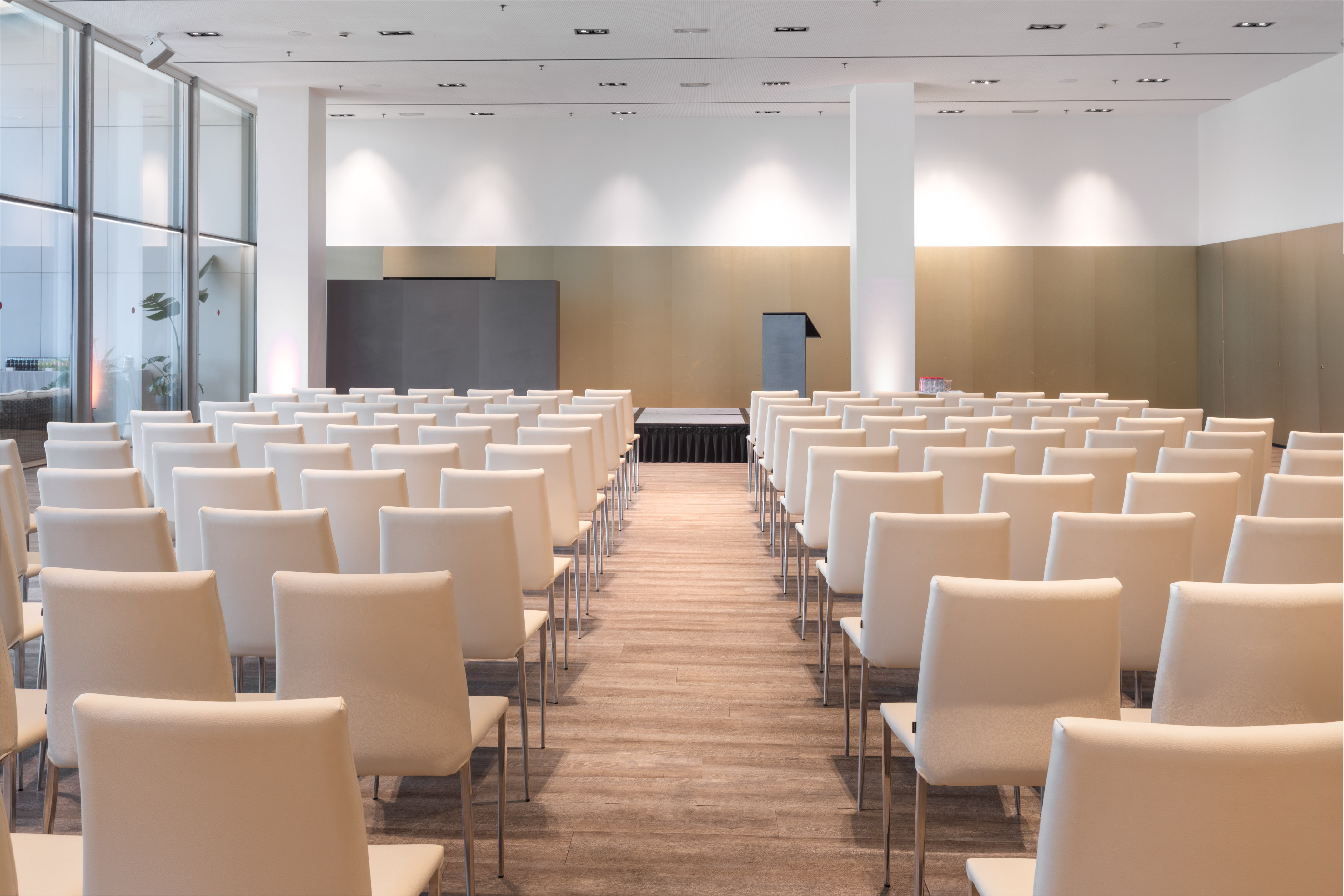 Spacious conference room with rows of white chairs, stage, and podium.