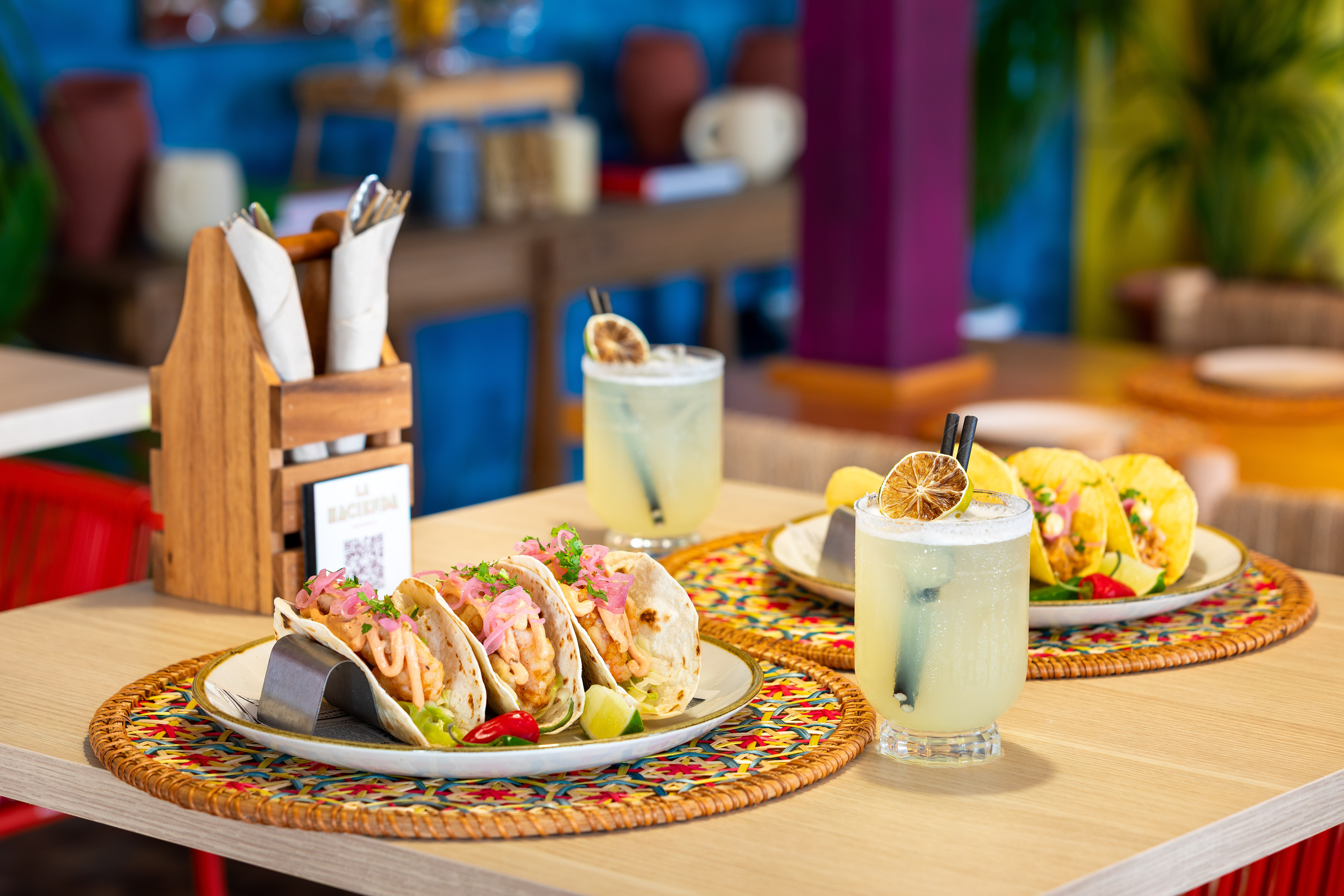 Fish tacos with pickled onions, lime, and two margaritas on a restaurant table.