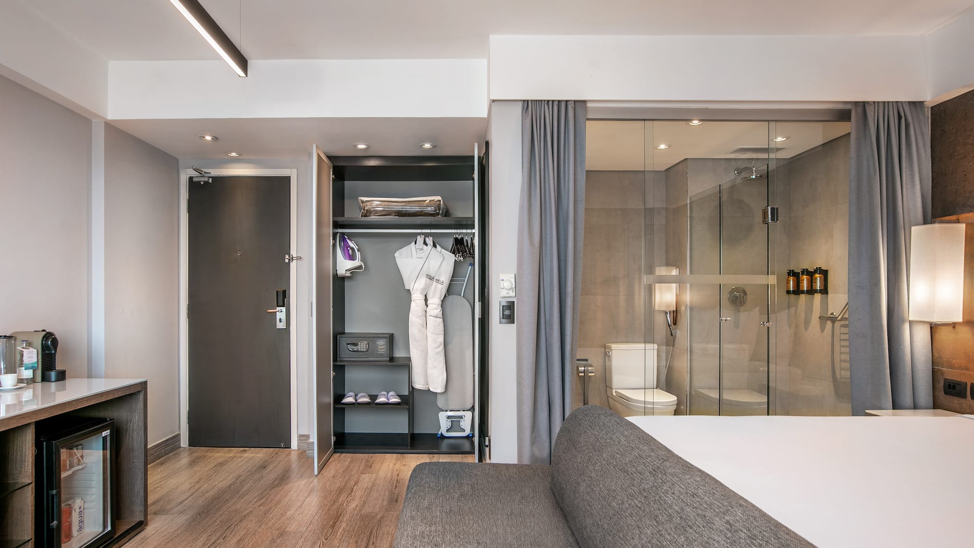 Quarto de hotel moderno com armário aberto, frigobar e banheiro de vidro. - Grand Premium - Meliá Ibirapuera, São Paulo