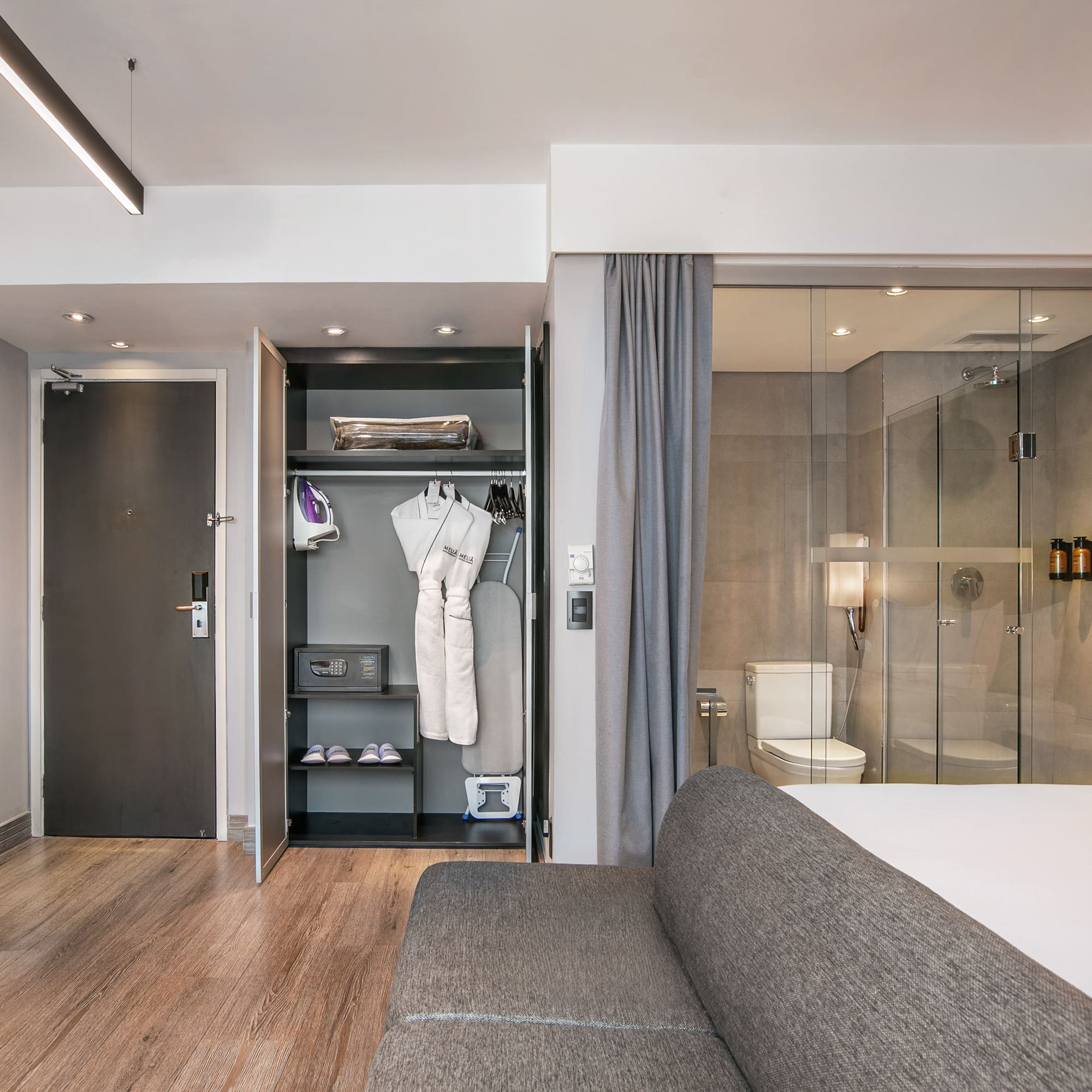 Quarto de hotel moderno com armário aberto, frigobar e banheiro de vidro. - Grand Premium - Meliá Ibirapuera, São Paulo