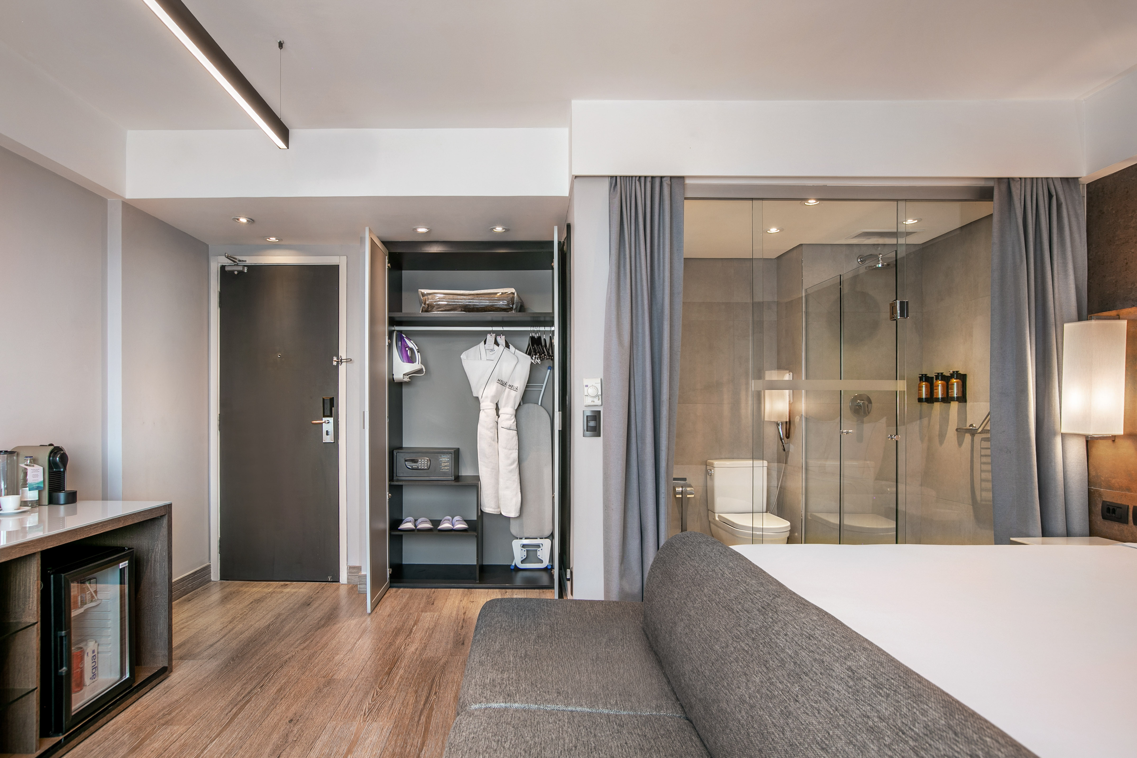 Quarto de hotel moderno com armário aberto, frigobar e banheiro de vidro. - Grand Premium - Meliá Ibirapuera, São Paulo