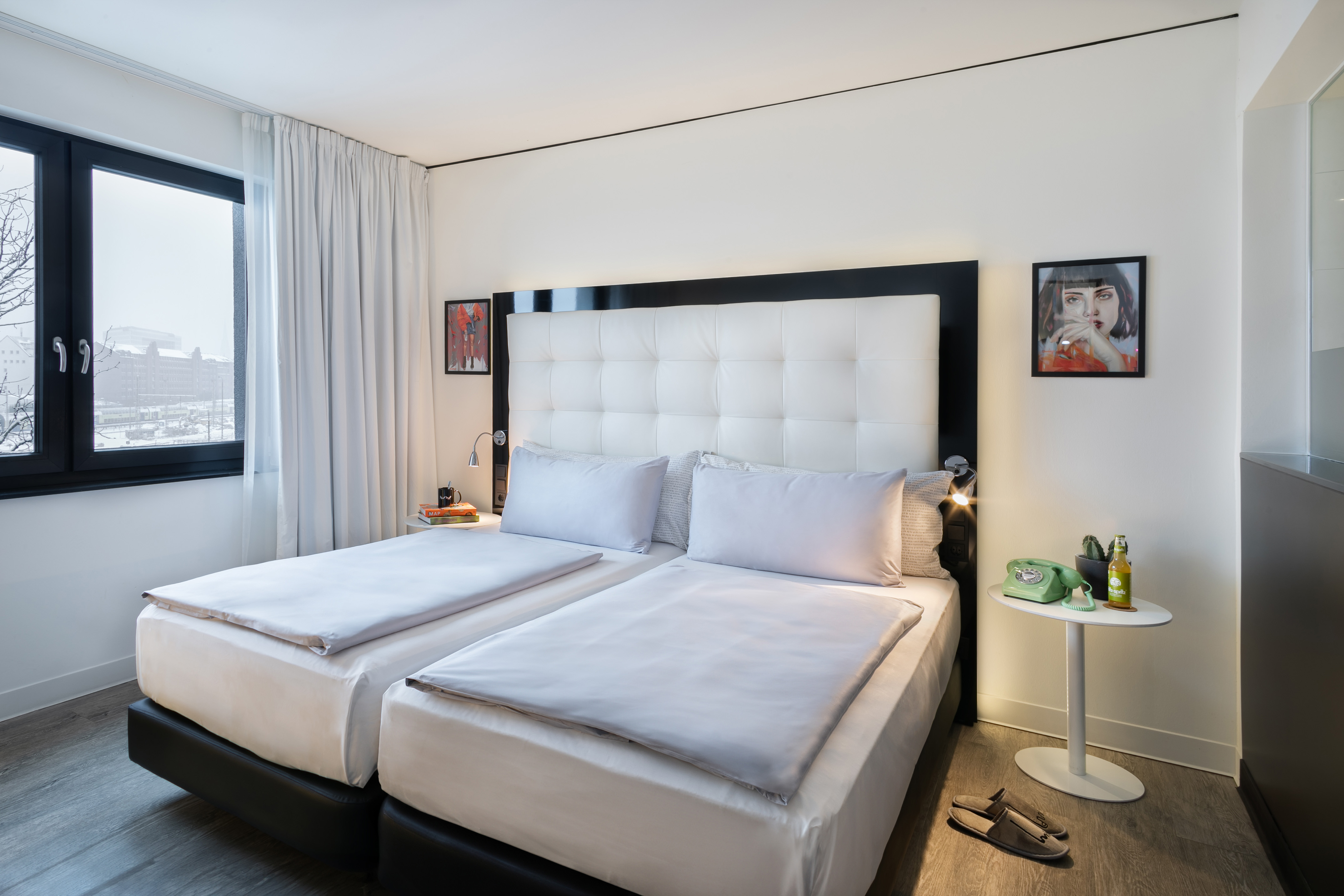 Hotel room with twin beds, white bedding, black headboard, cityscape view.