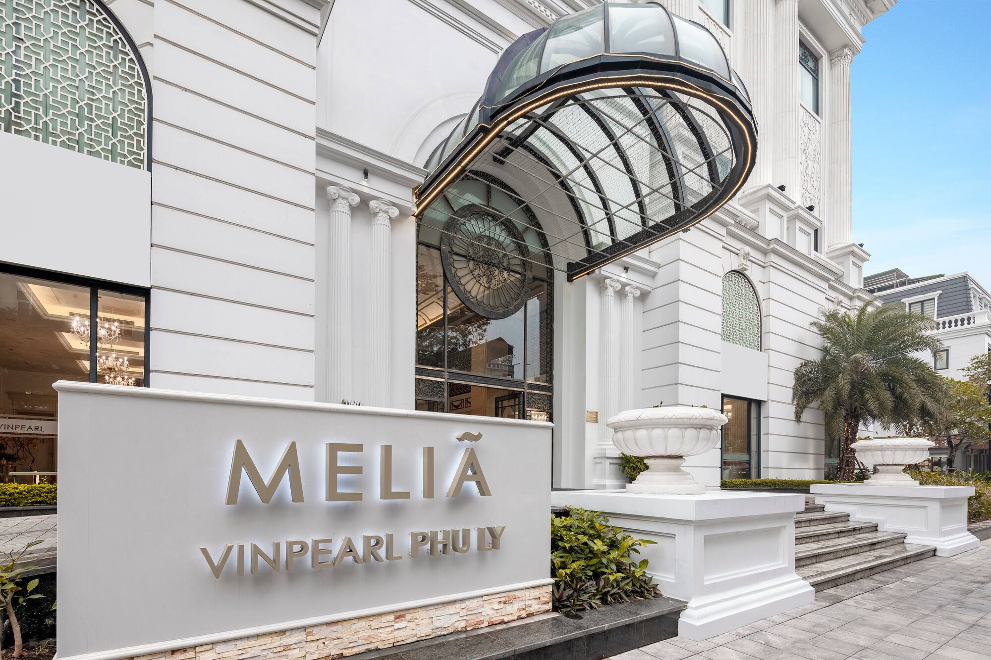 Melia Vinpearl Phu Ly hotel entrance with white facade and modern glass canopy.