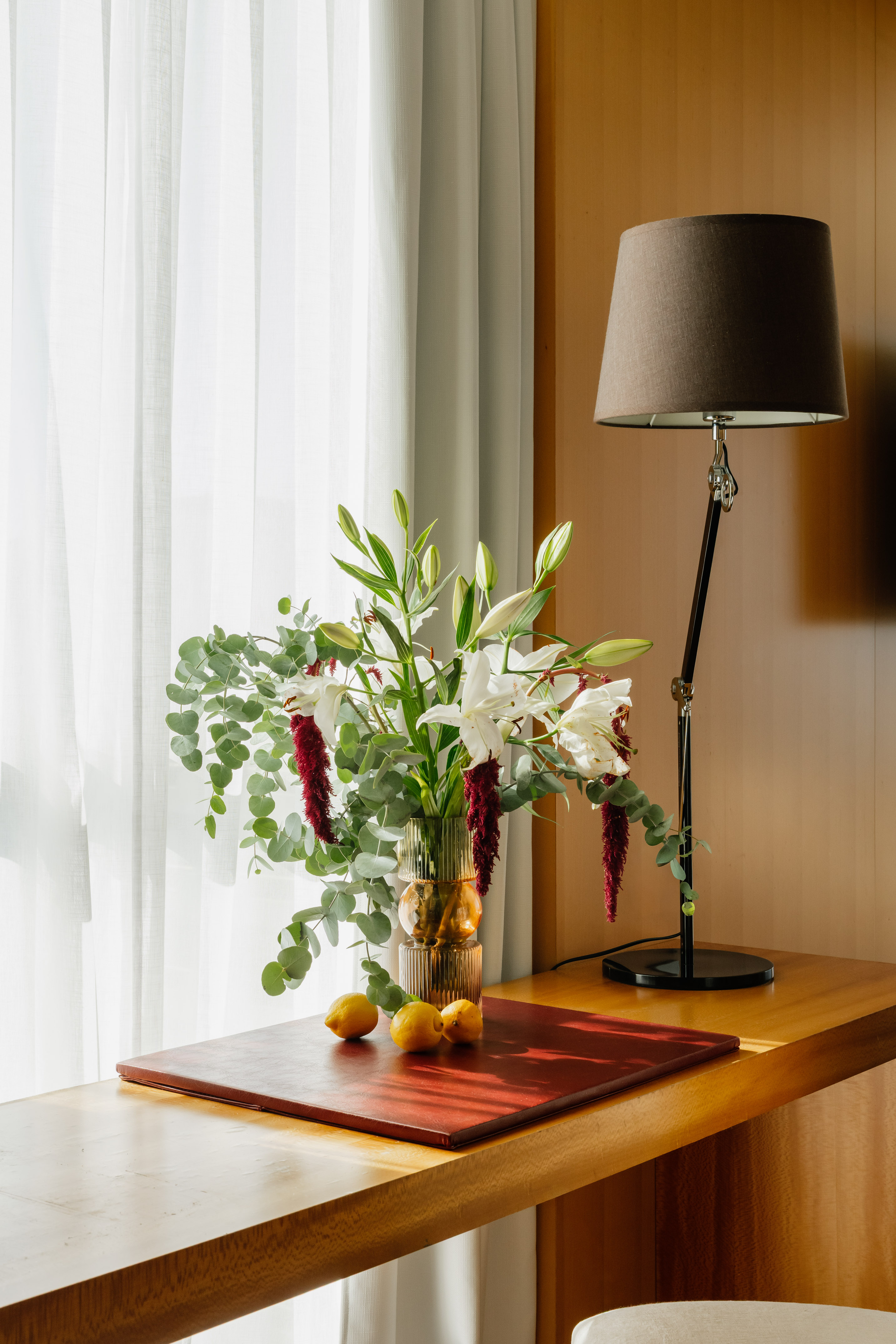 Hotel desk with white lily and eucalyptus bouquet, lemons, and modern lamp.