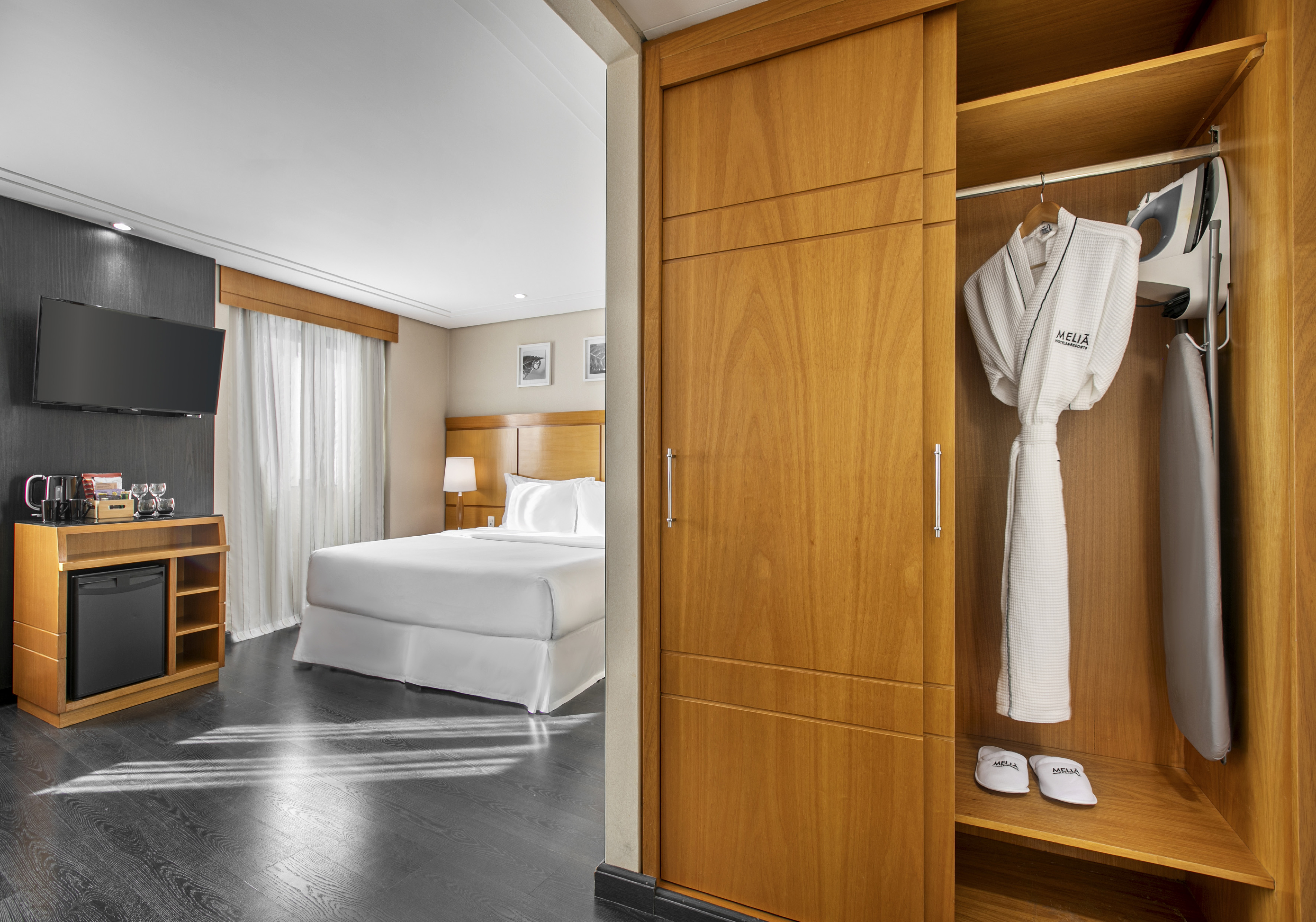 Meliã hotel room with open closet, bathrobe, iron, slippers, bed, and minibar.