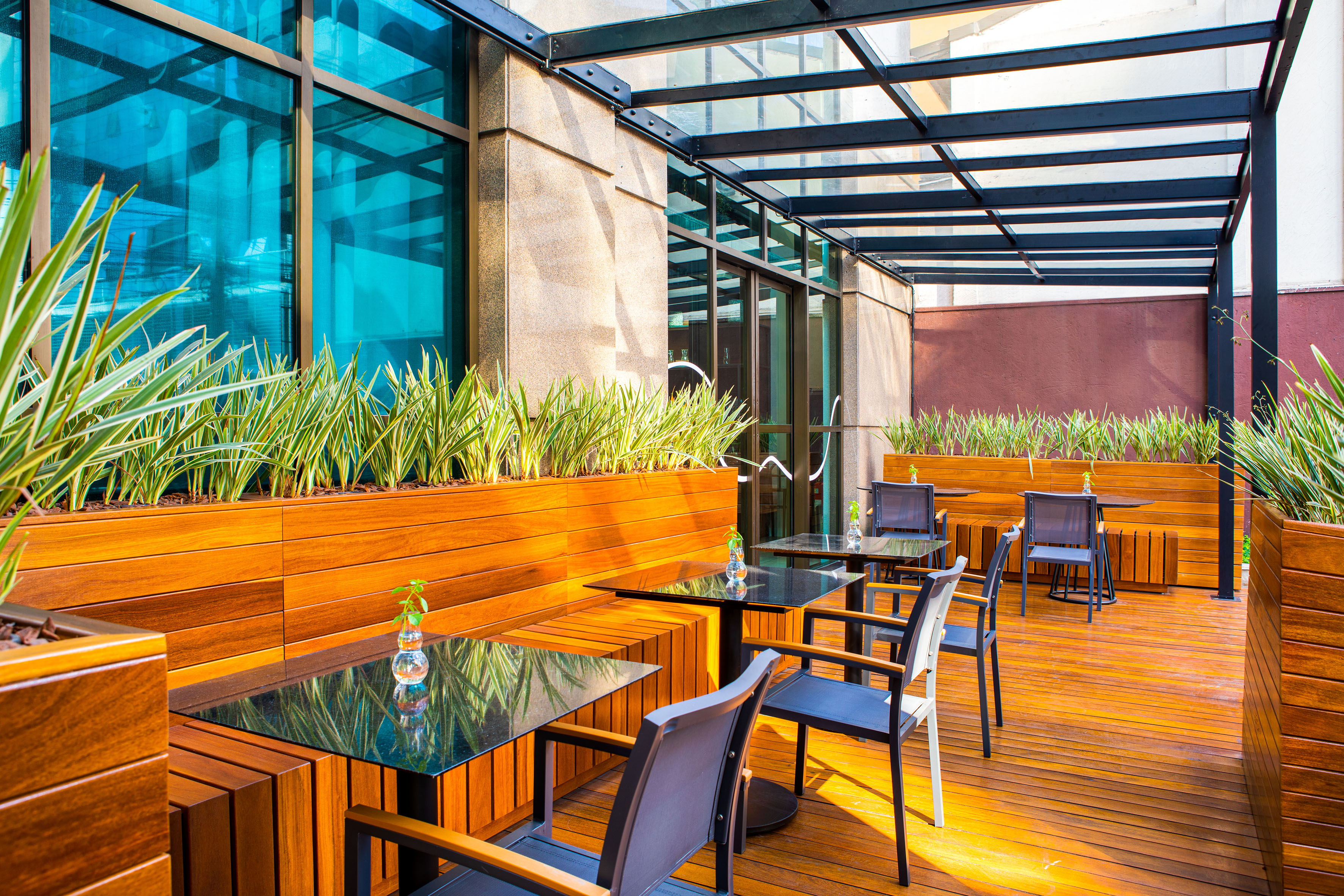 Modern outdoor cafe patio with wooden deck, green planters, tables, and chairs.