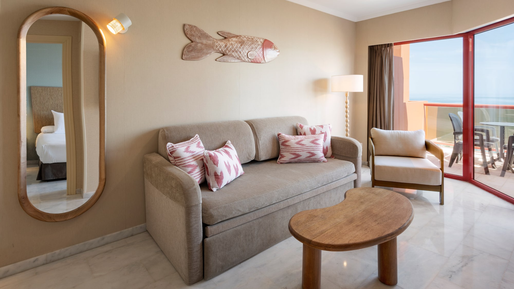 Hotel suite living room with sofa, ocean view balcony, and mirror.