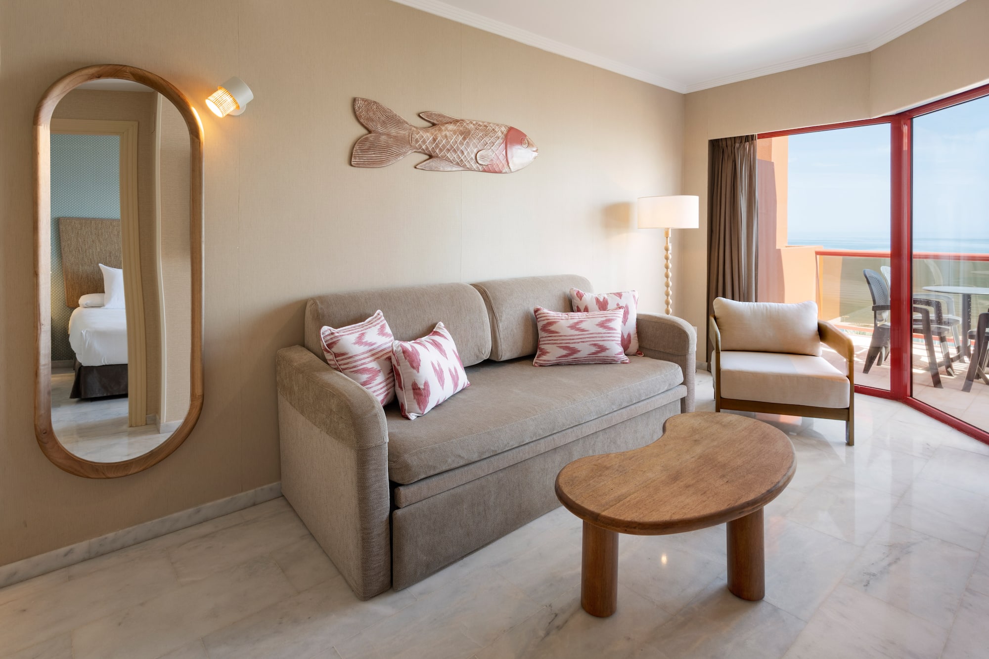 Hotel suite living room with sofa, mirror, and ocean view balcony.