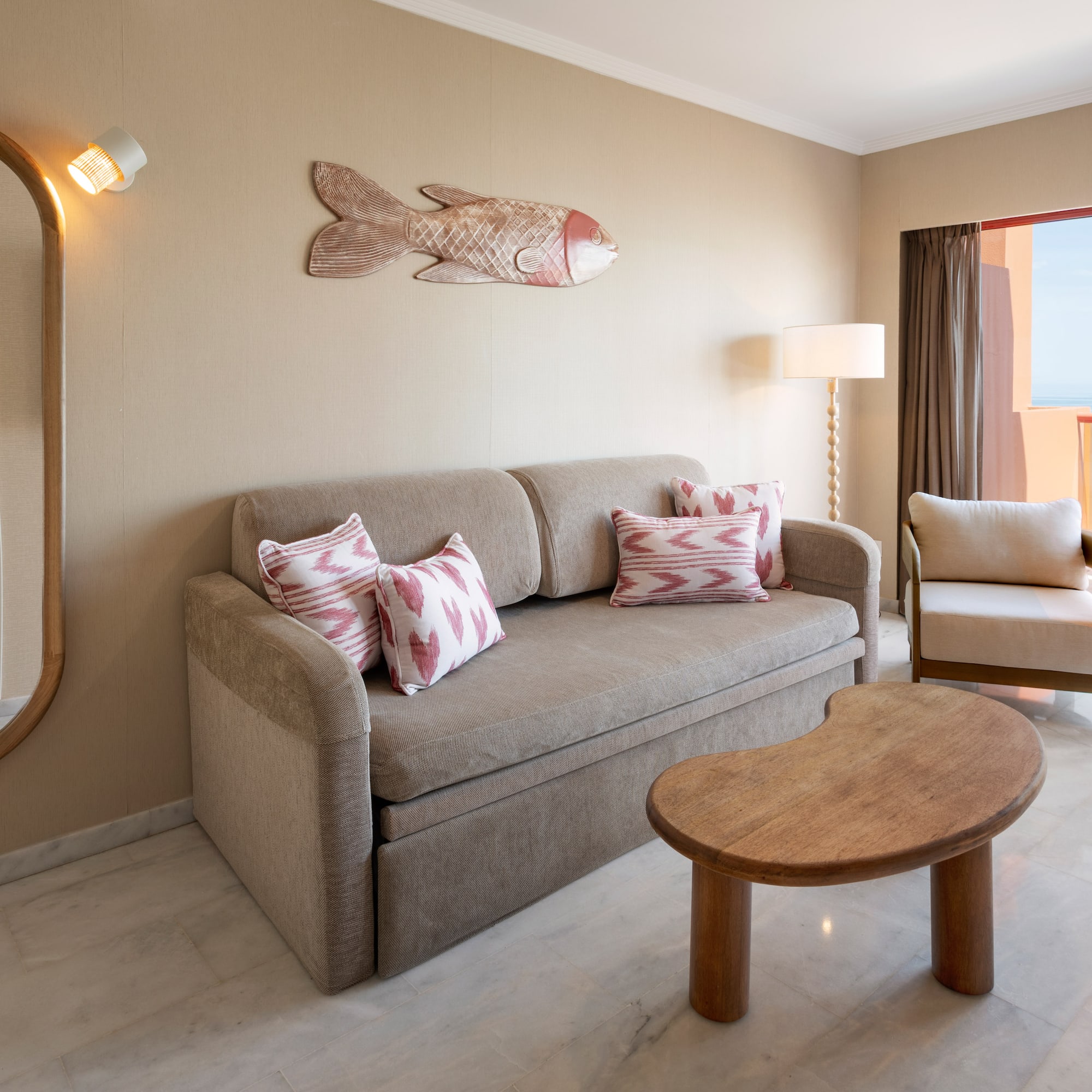 Hotel suite living room with sofa, ocean view balcony, and mirror.
