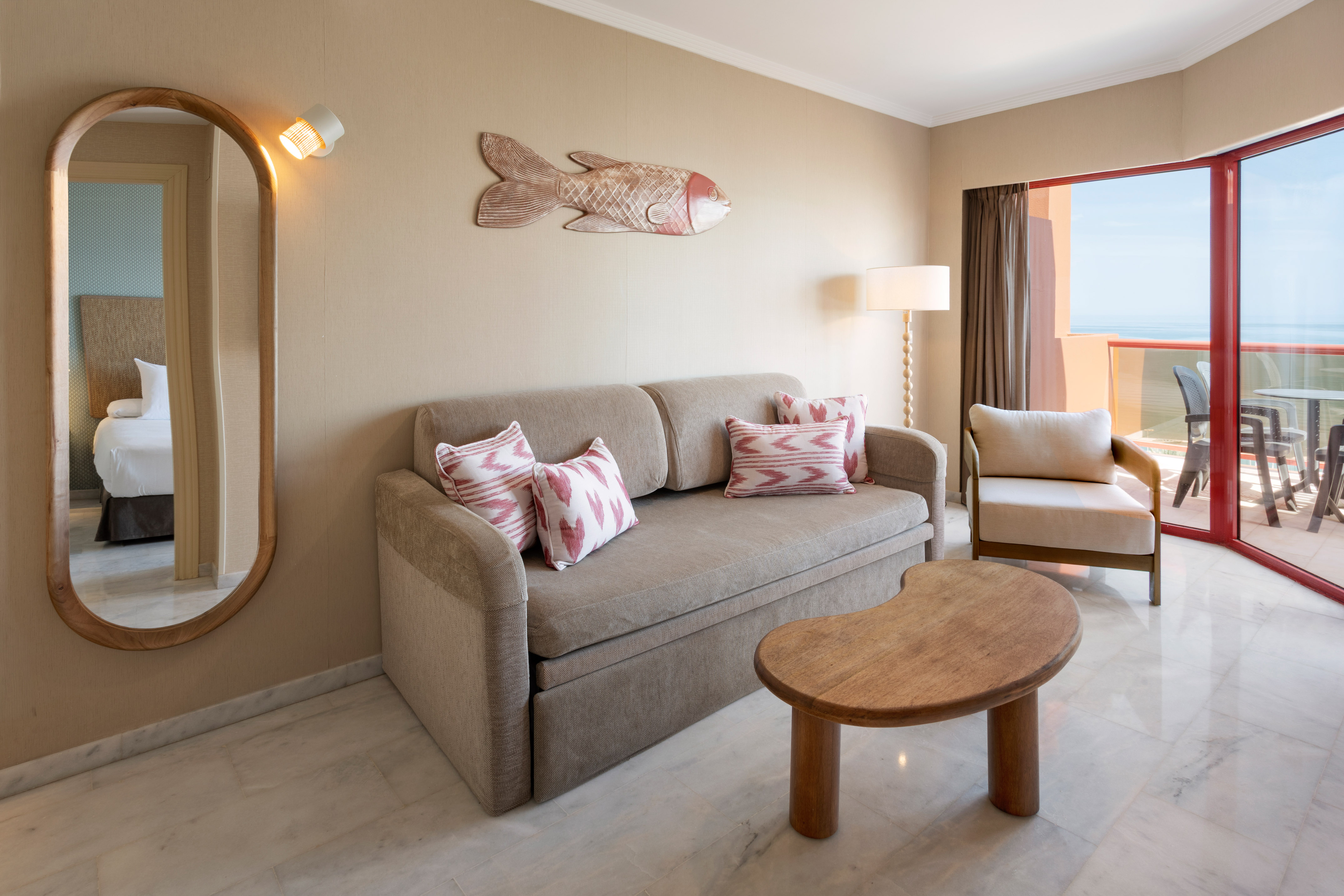 Hotel suite living room with sofa, ocean view balcony, and mirror.
