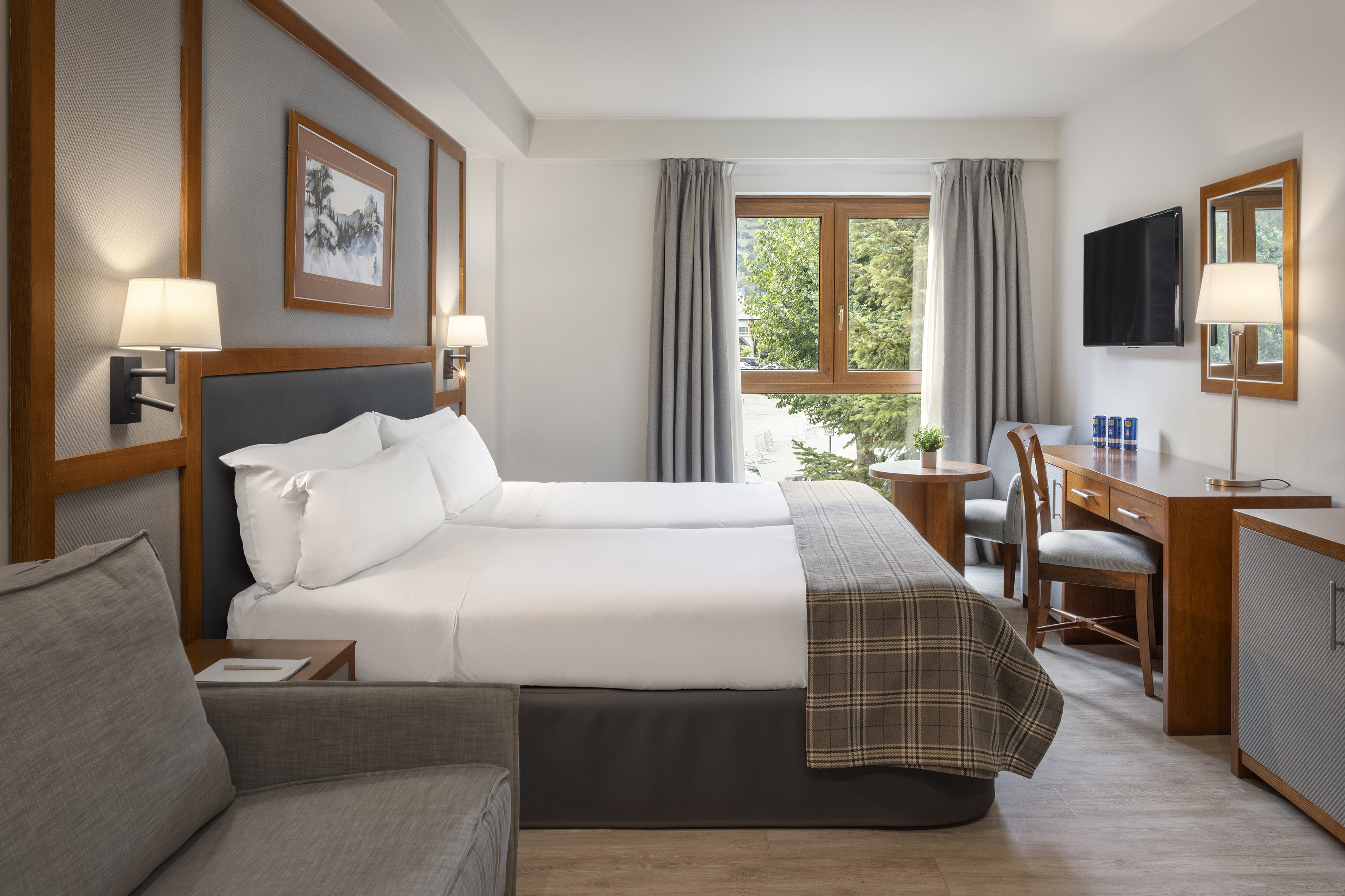 Cozy hotel room with twin beds, wooden desk, and a window overlooking trees.